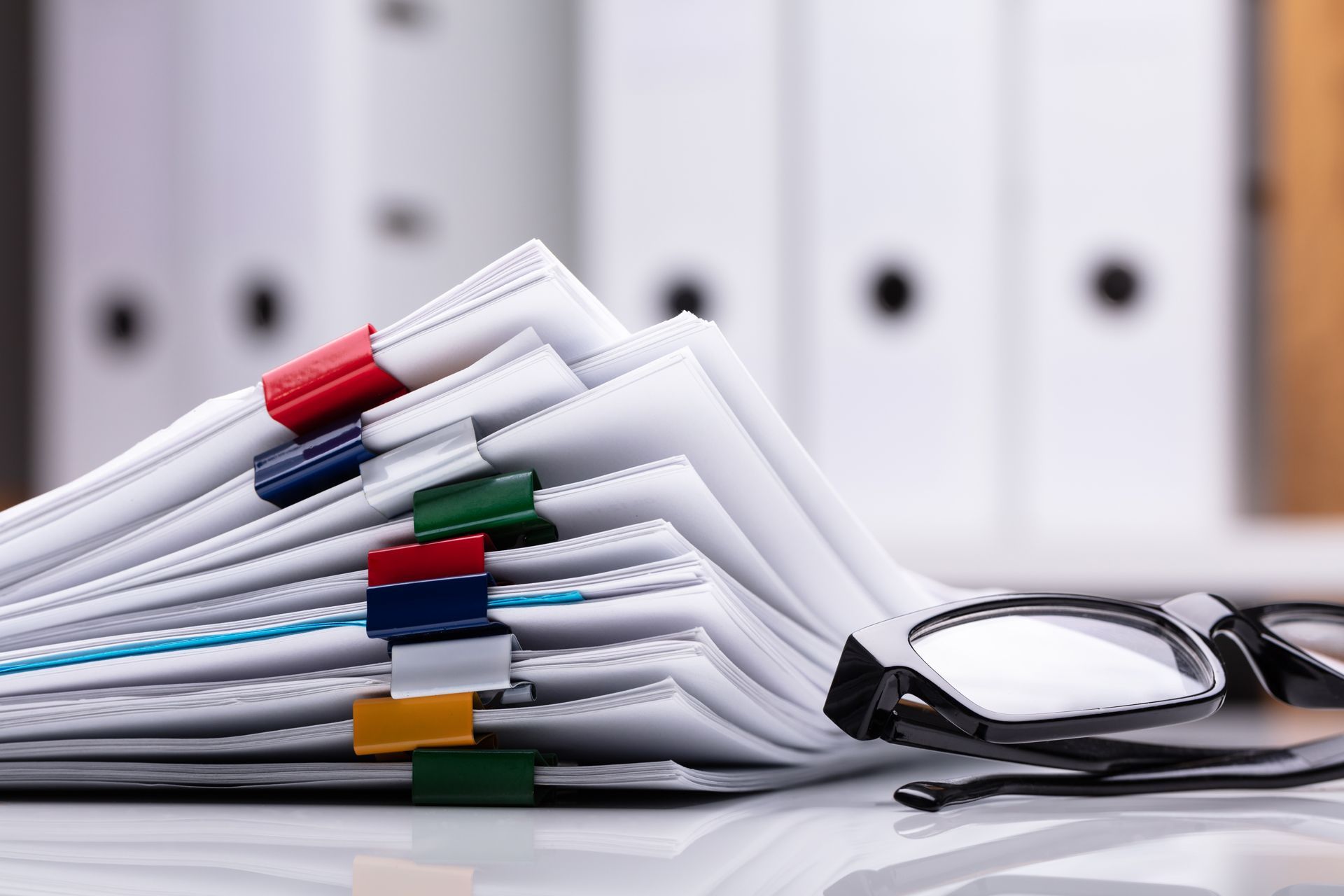 Stack of binders with colored tabs beside eyeglasses on a desk