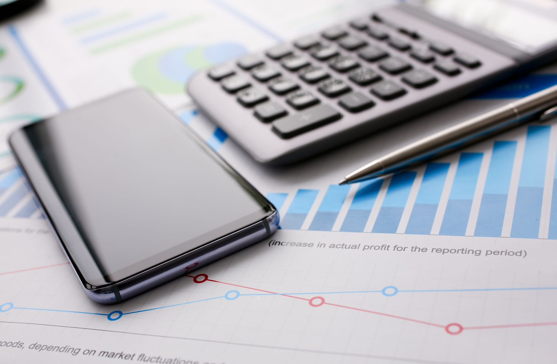 Smartphone, calculator, and pen on financial charts with blue upward graph line