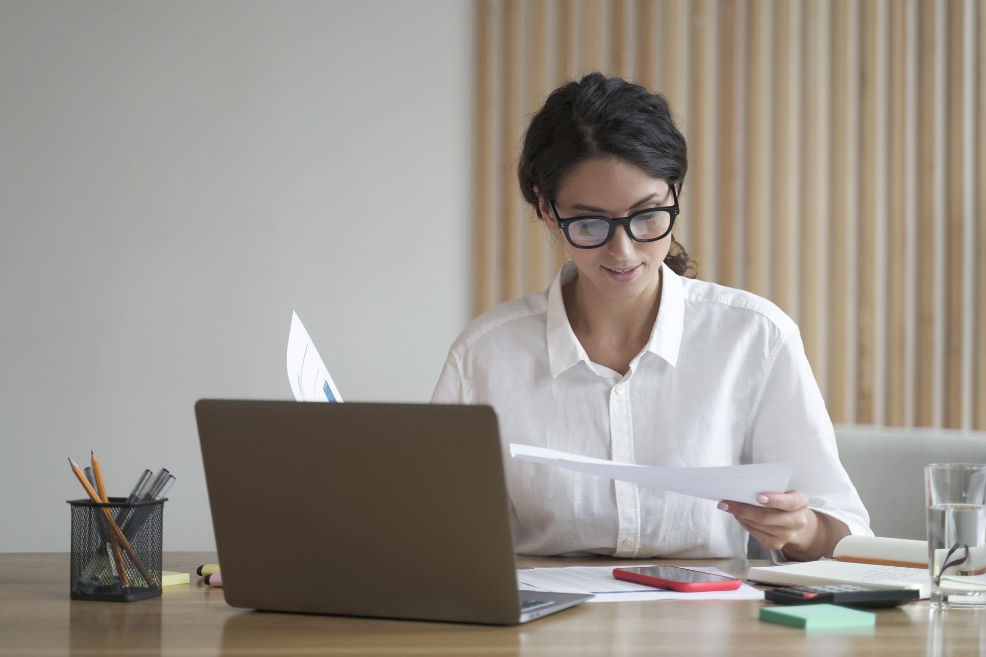 Person reviewing papers at a desk with a laptop in a bright office