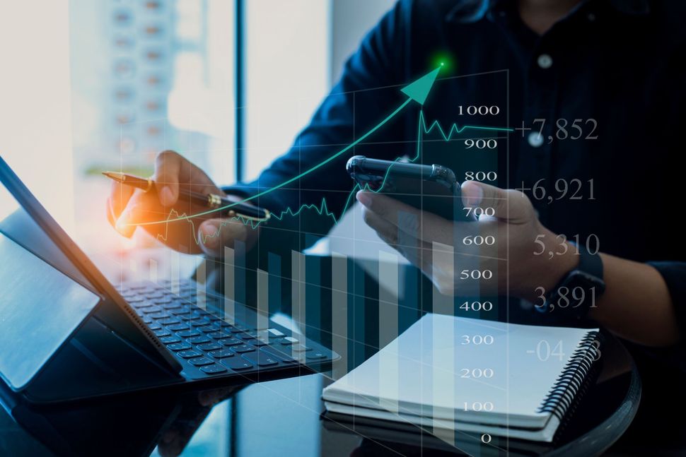 Businessperson using laptop with financial charts and data overlay in a modern office