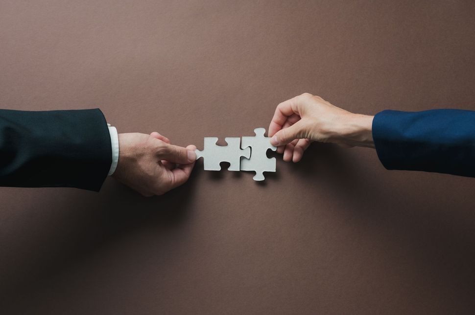 Two hands from opposite sides connect a white puzzle piece on a brown background