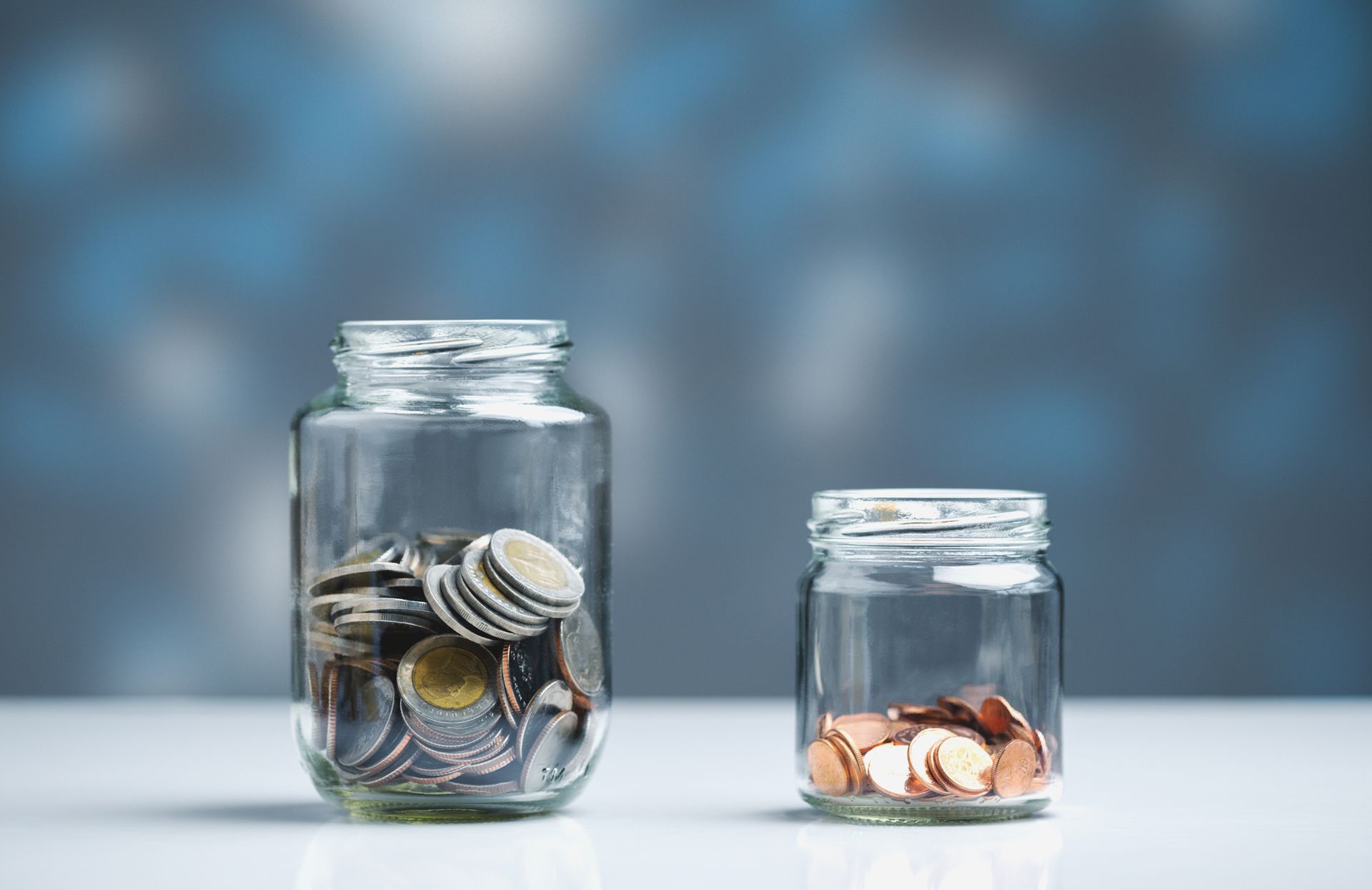 Two glass jars with coins, one full and one with a few pennies, on a white surface