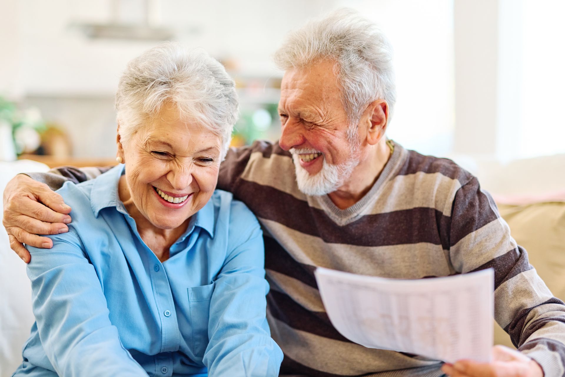 Smiling older couple sitting together on a couch, looking at a document and embracing.