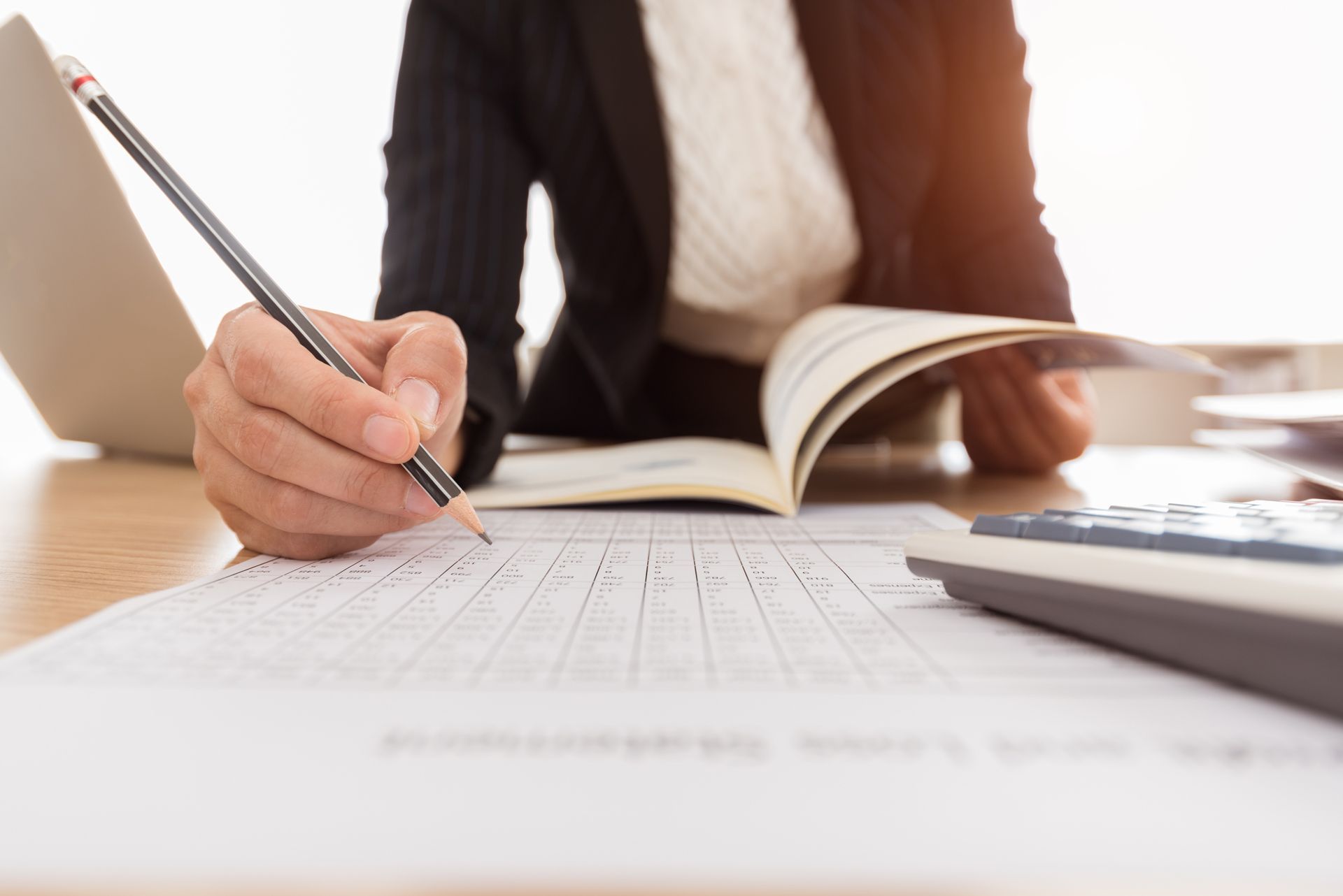 Person writing on a worksheet at a desk beside an open book and laptop