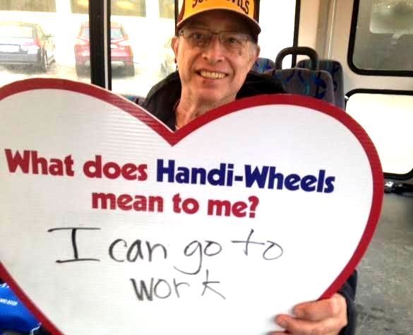 A male holding a heart with these written words: What does Handi-Wheels mean to me? I can go to work.