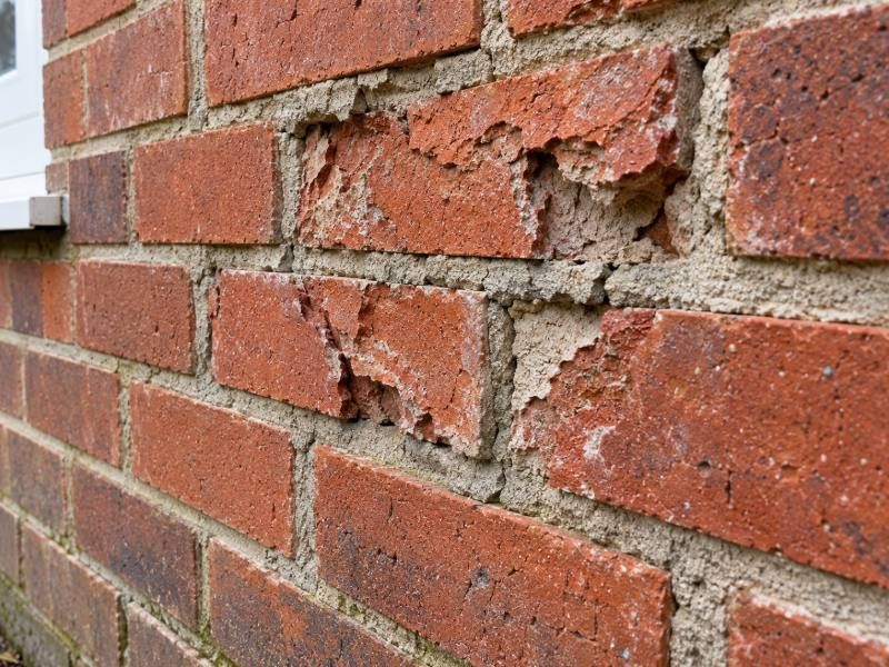 Spalled and frost damaged bricks in a wall marked up for cutting out