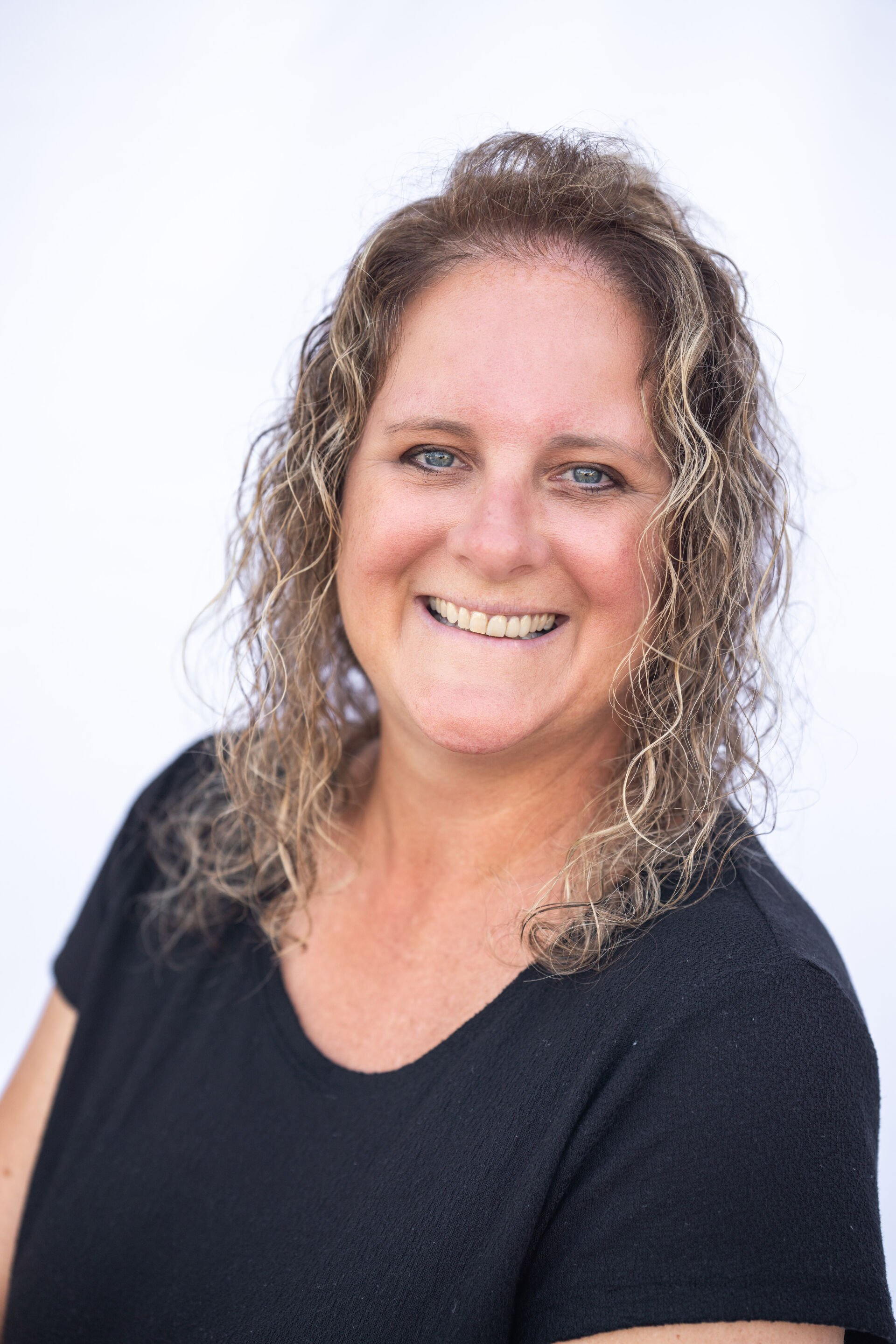 Smiling woman with curly hair in a black top against a white background
