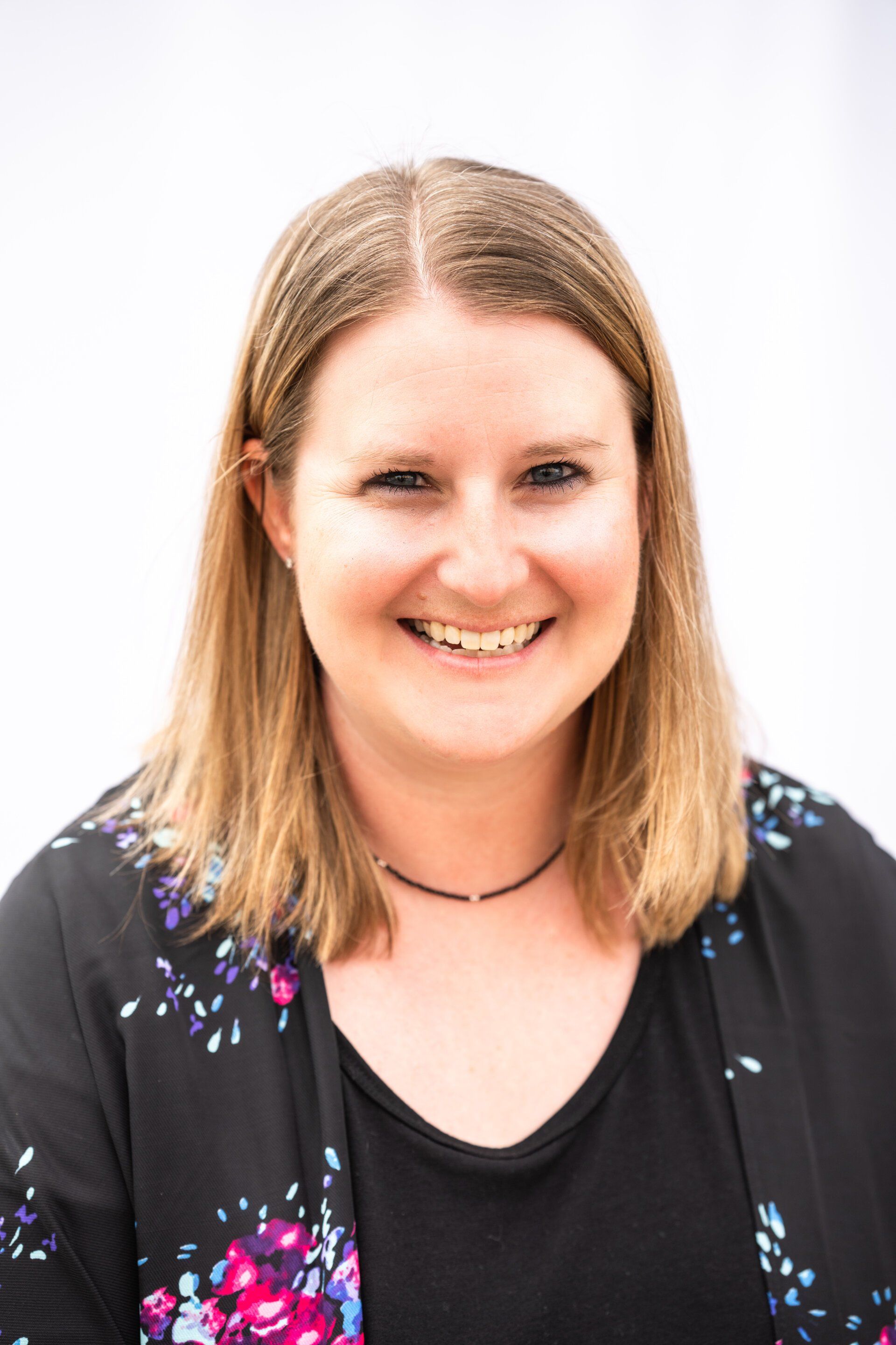 Smiling person with shoulder-length hair wearing a black top with floral accents on a white background
