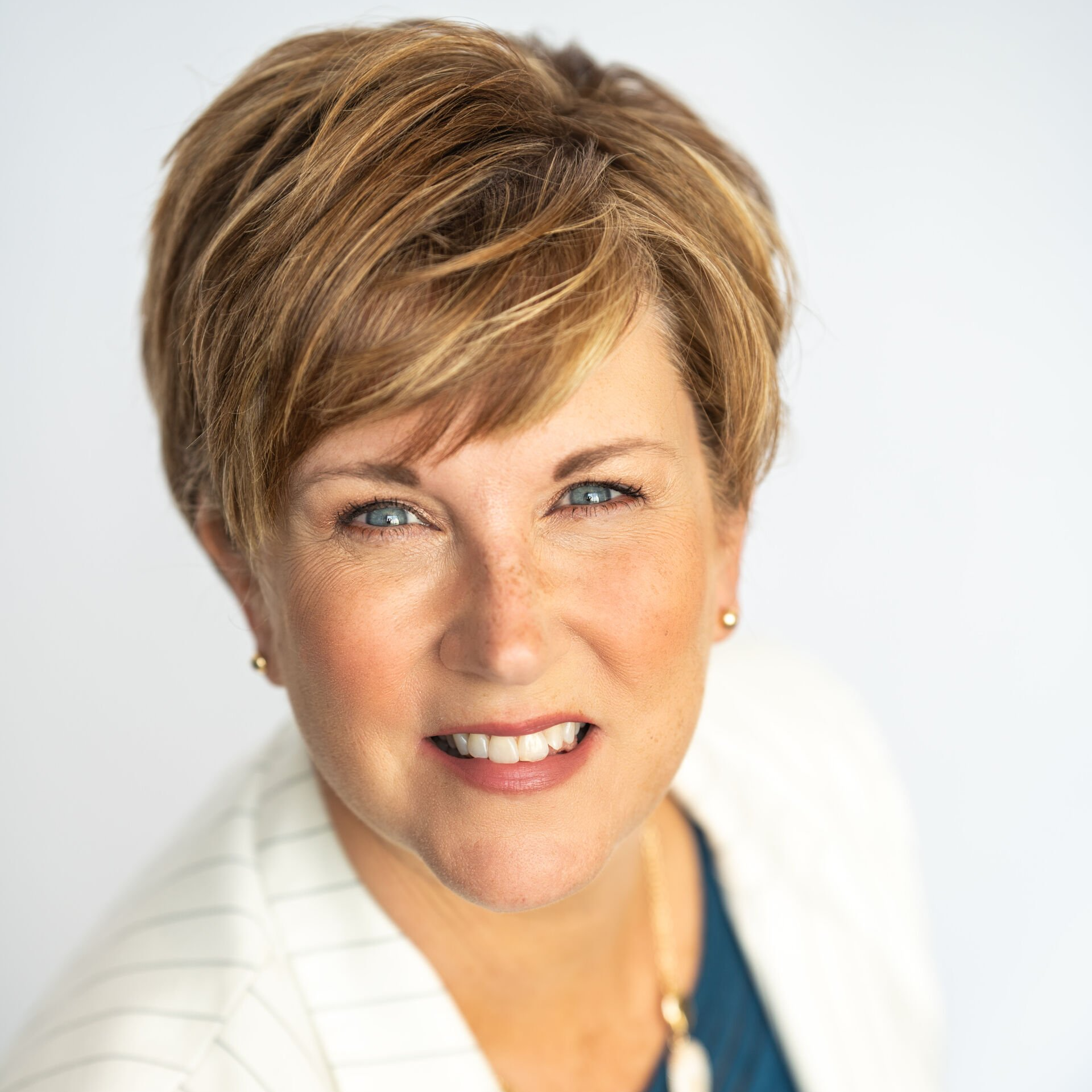 Portrait of a smiling woman with short brown hair in a white blazer against a light background