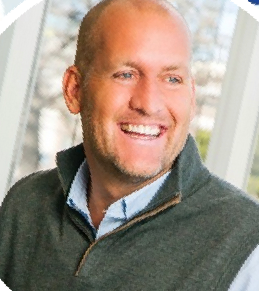 Smiling man in a dark green sweater standing by a bright window
