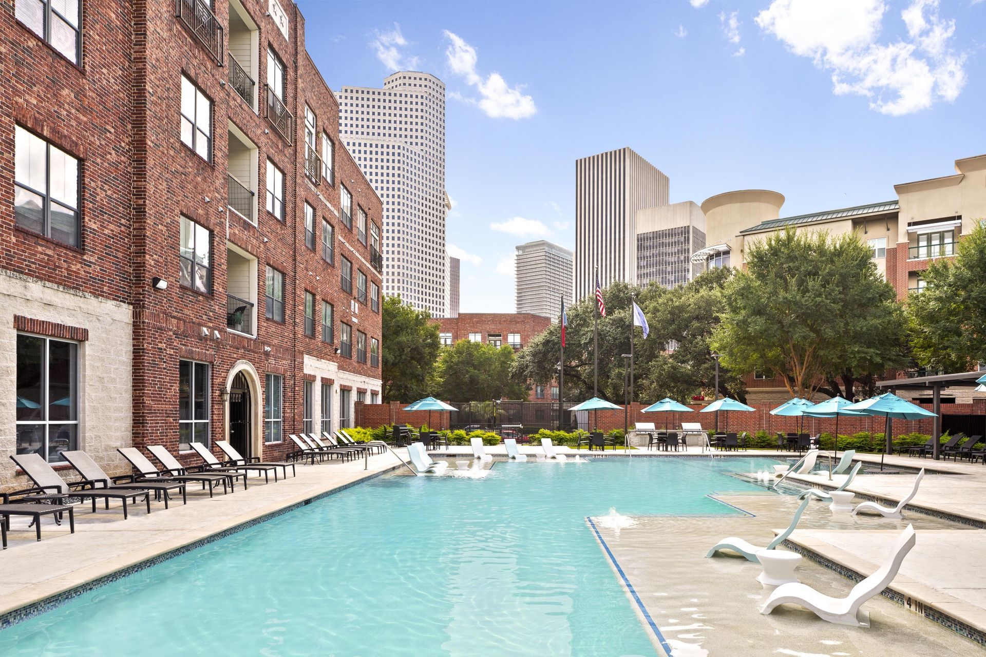 Swimming pool with lounge chairs and umbrellas near a residential building at Marquis Enclave, offers apartments near Citycentre in Houston, TX.