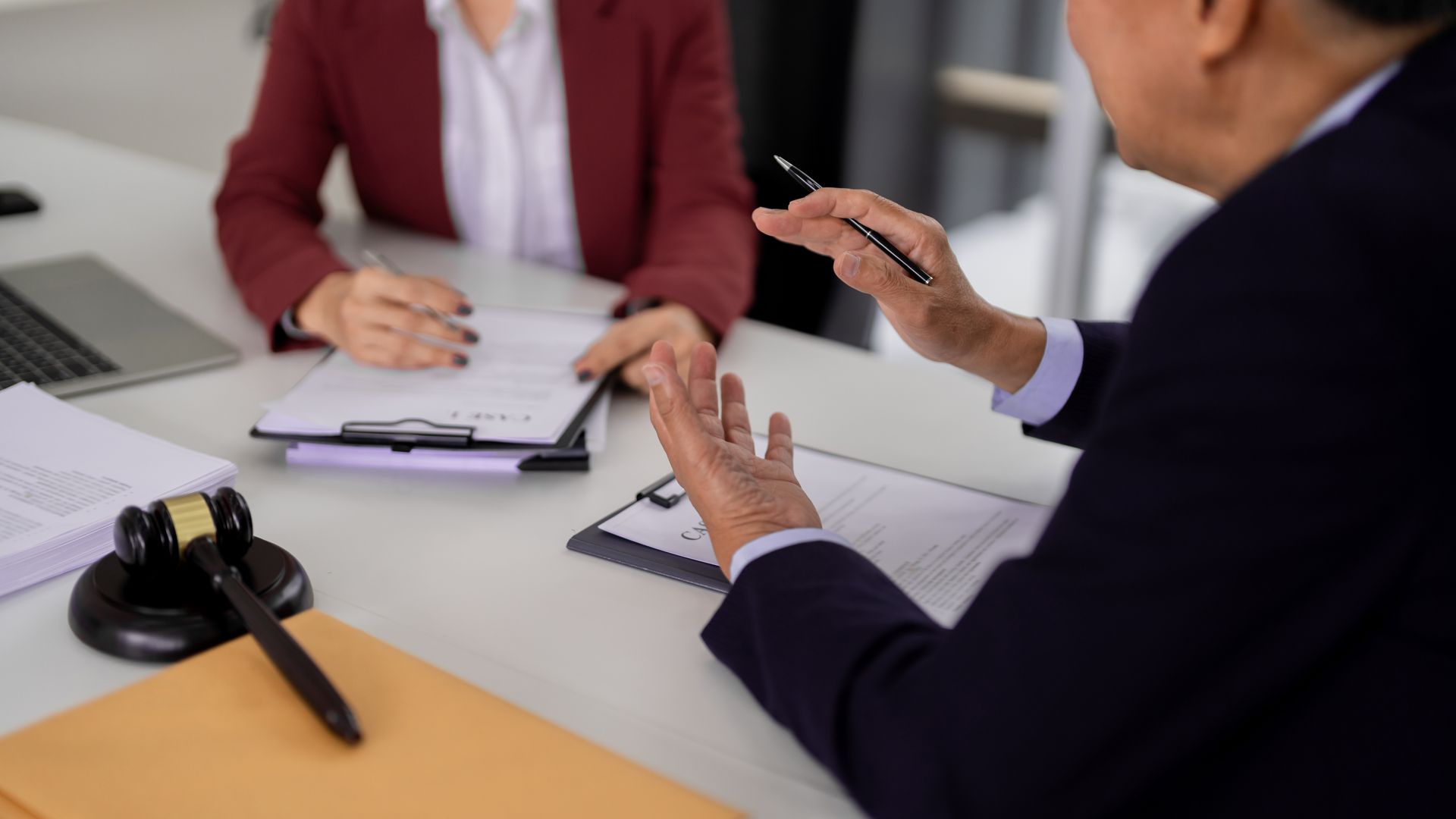 Zwei Personen in einer Besprechung, die über Papierkram auf einem Schreibtisch mit Konferenztelefon gestikulieren.
