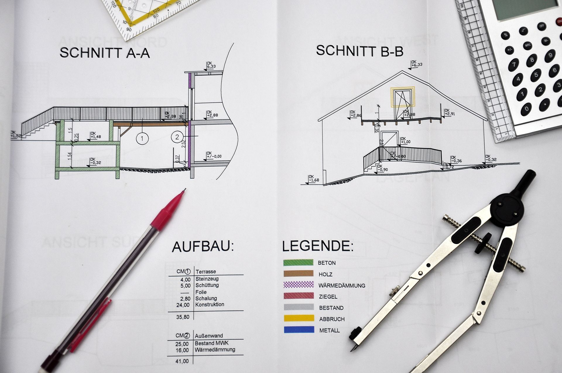 Architektonischer Bauplan mit Schnitten, farbiger Legende, rotem Stift und Zirkel auf einem weißen Schreibtisch