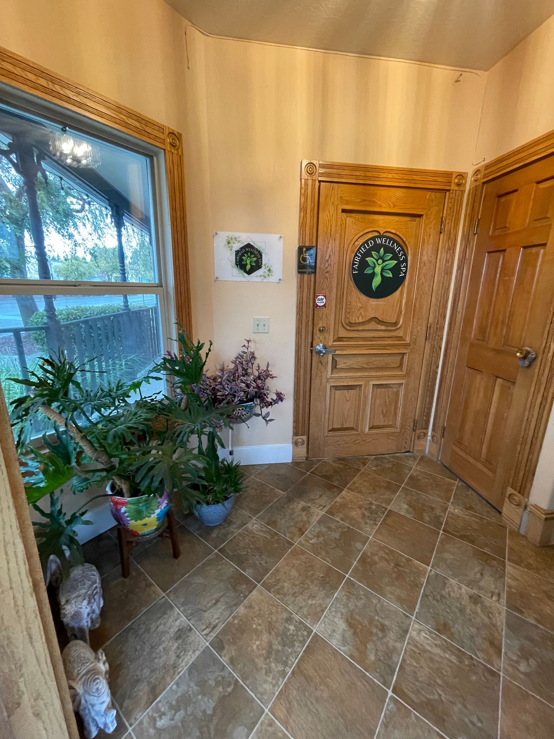 Small entryway with tile floor, wood doors, potted plants, and a large window.