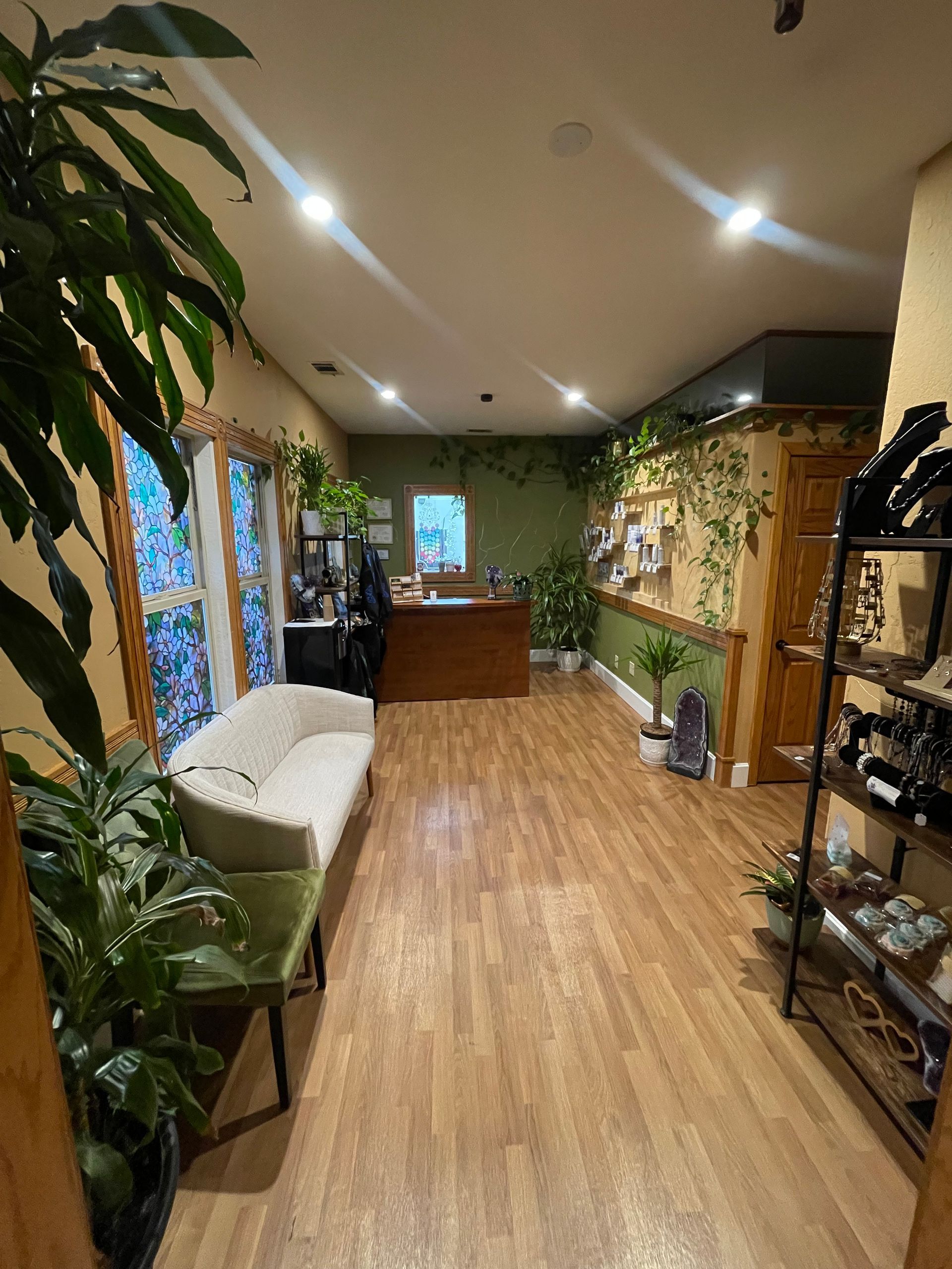 Bright, plant-filled hallway with wood floors, bench seating, and a small desk at the far end.