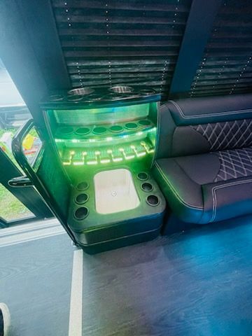 LED-lit cup holder and storage area beside patterned bus seats under a window.