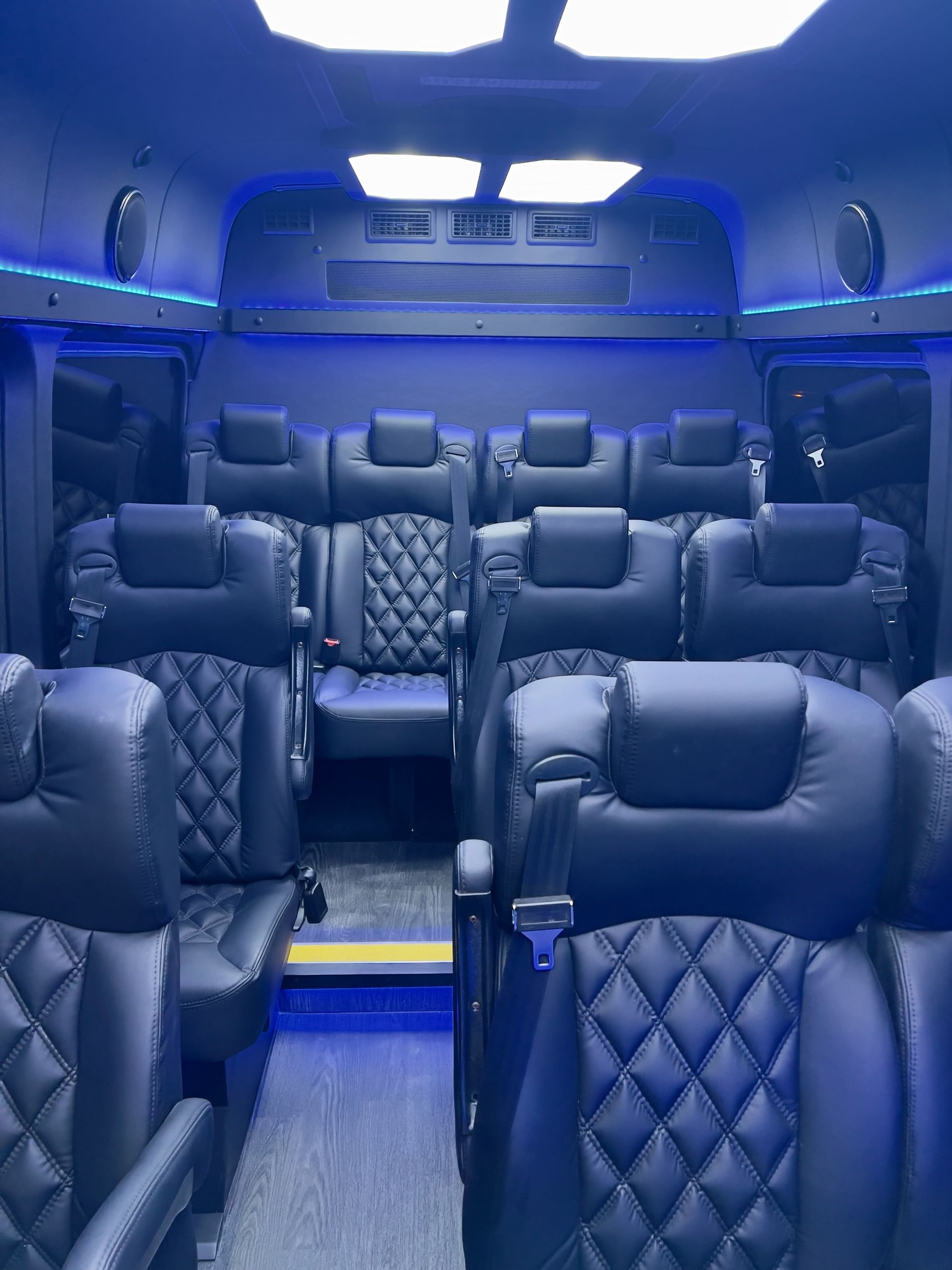 Blue-lit luxury van interior with quilted leather seats and a central aisle