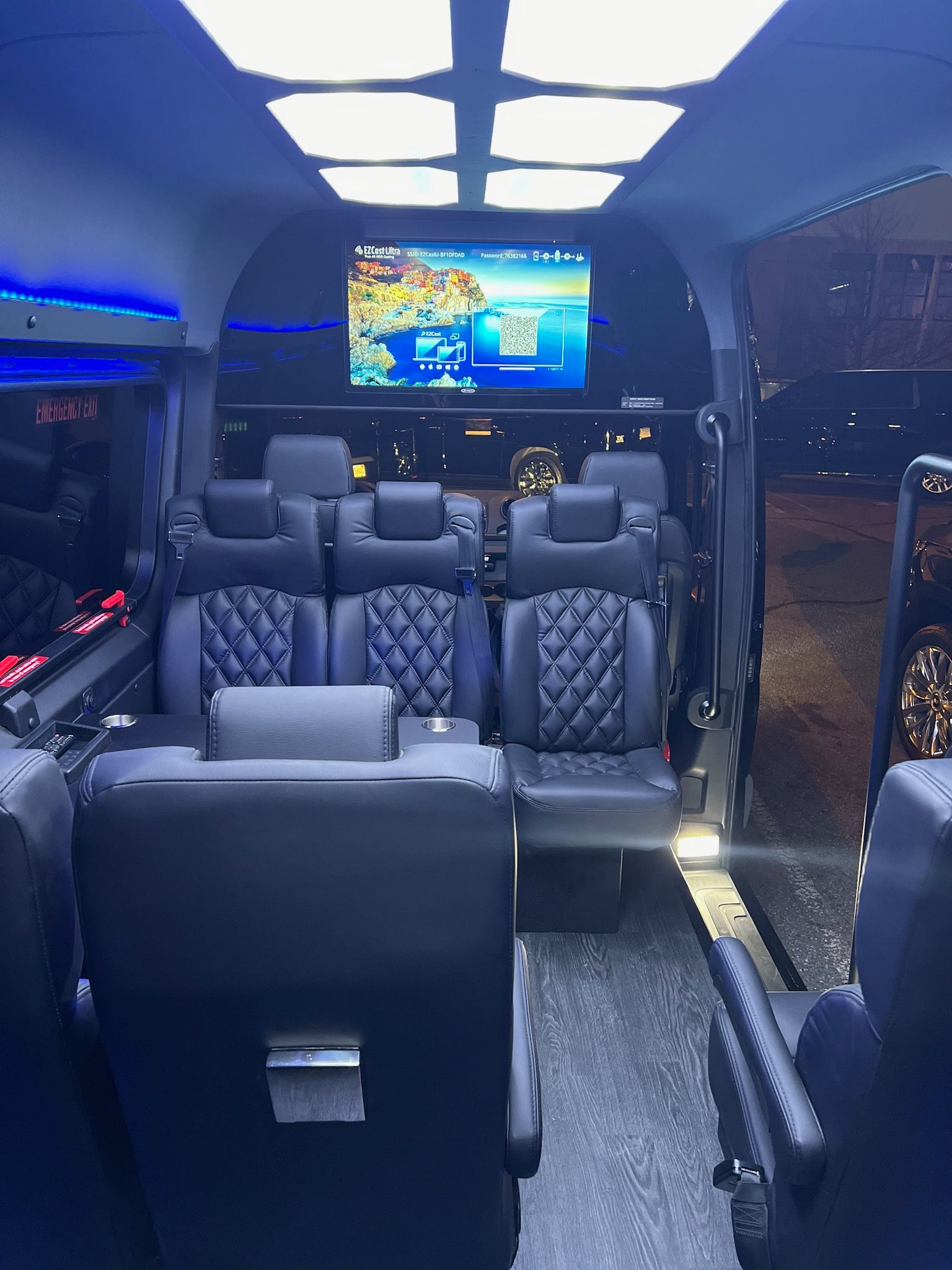 Interior of a luxury party bus with blue lighting, black leather seats, and a TV at the front.