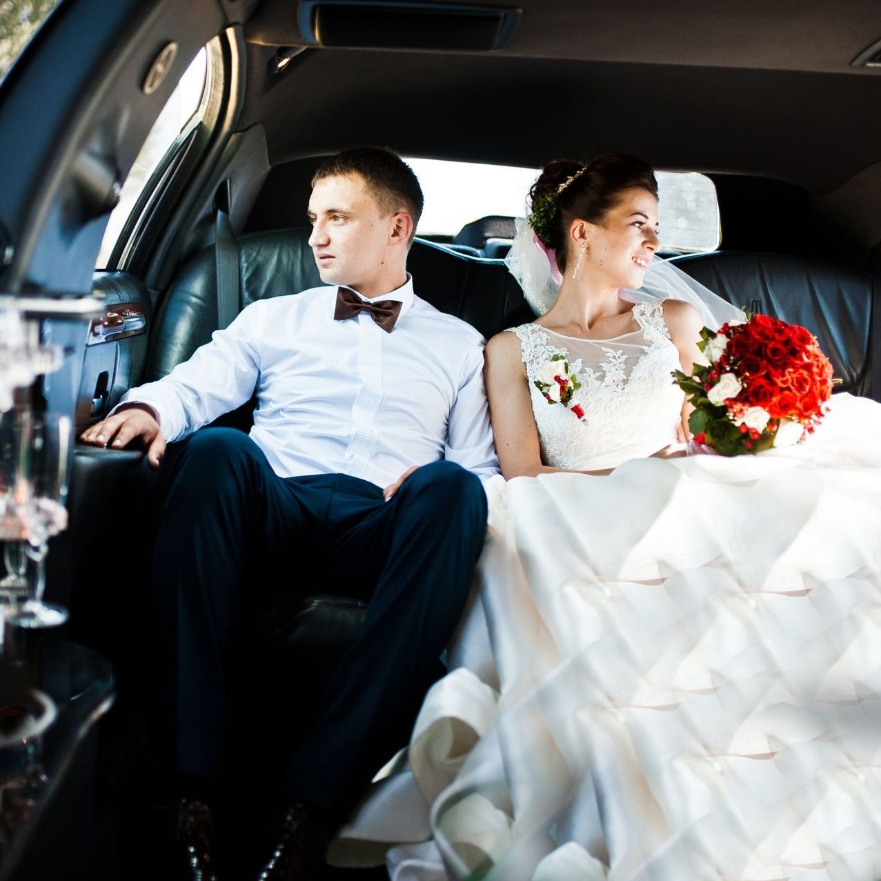 Bride and groom seated in a limousine, the bride holding a red bouquet and looking out the window