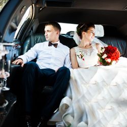 Bride and groom seated in a limousine, the bride holding a red bouquet and looking out the window