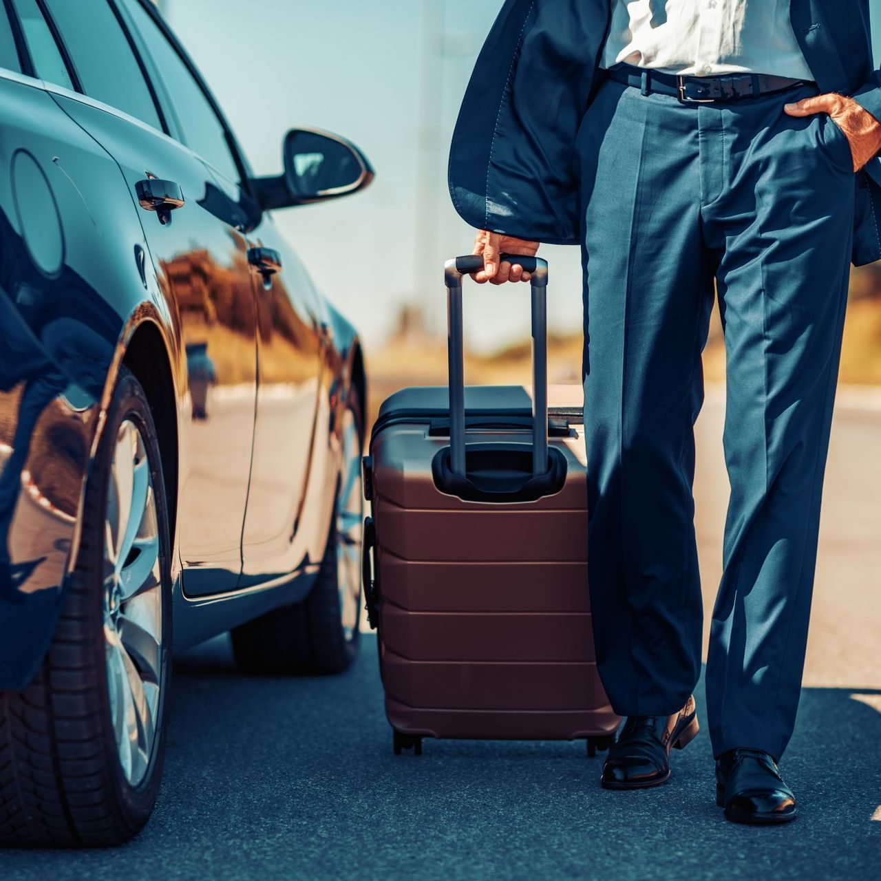 Traveler pulling a brown suitcase beside a parked car on a road