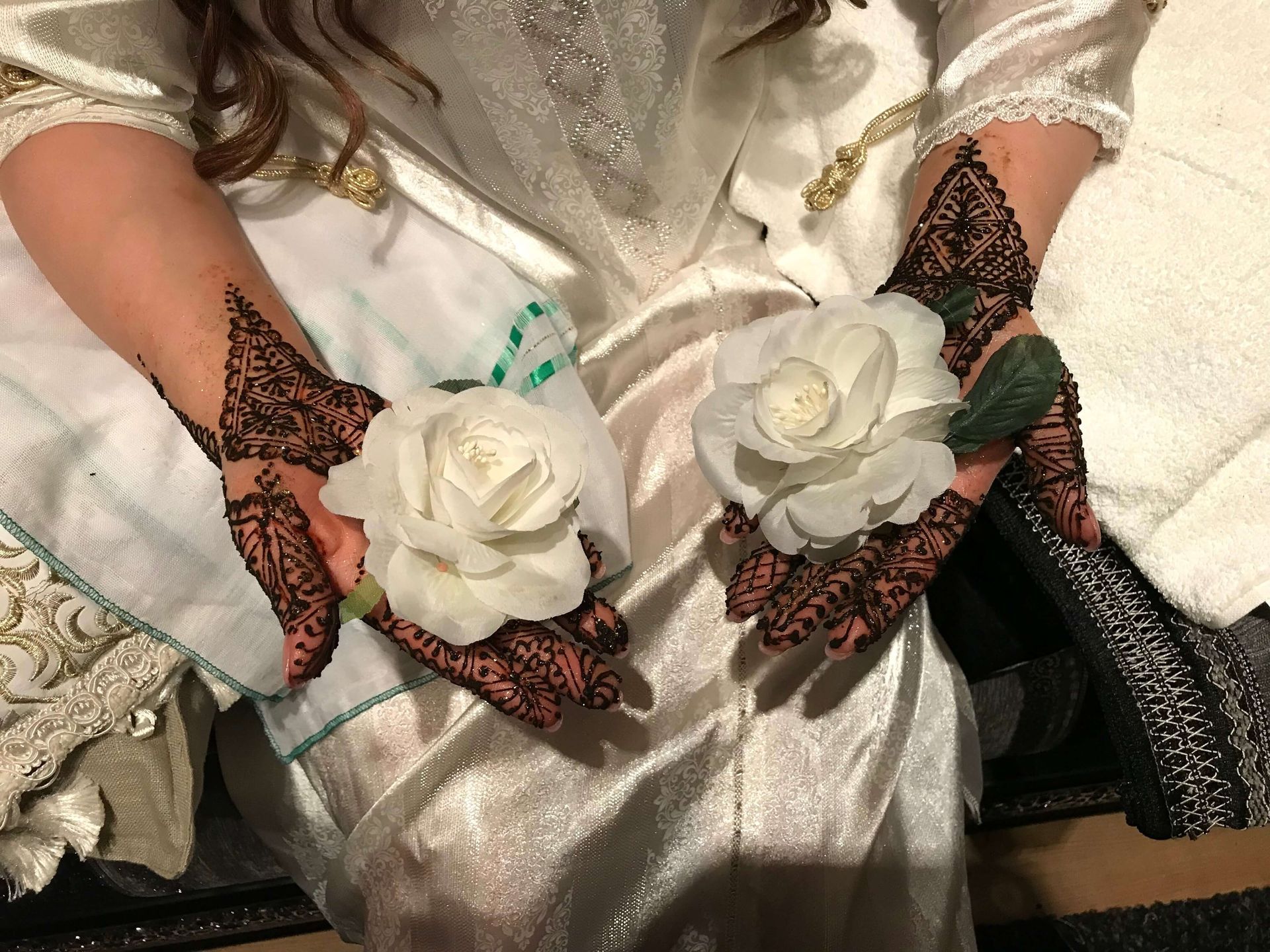 Een vrouw met henna op haar handen houdt twee witte rozen vast.