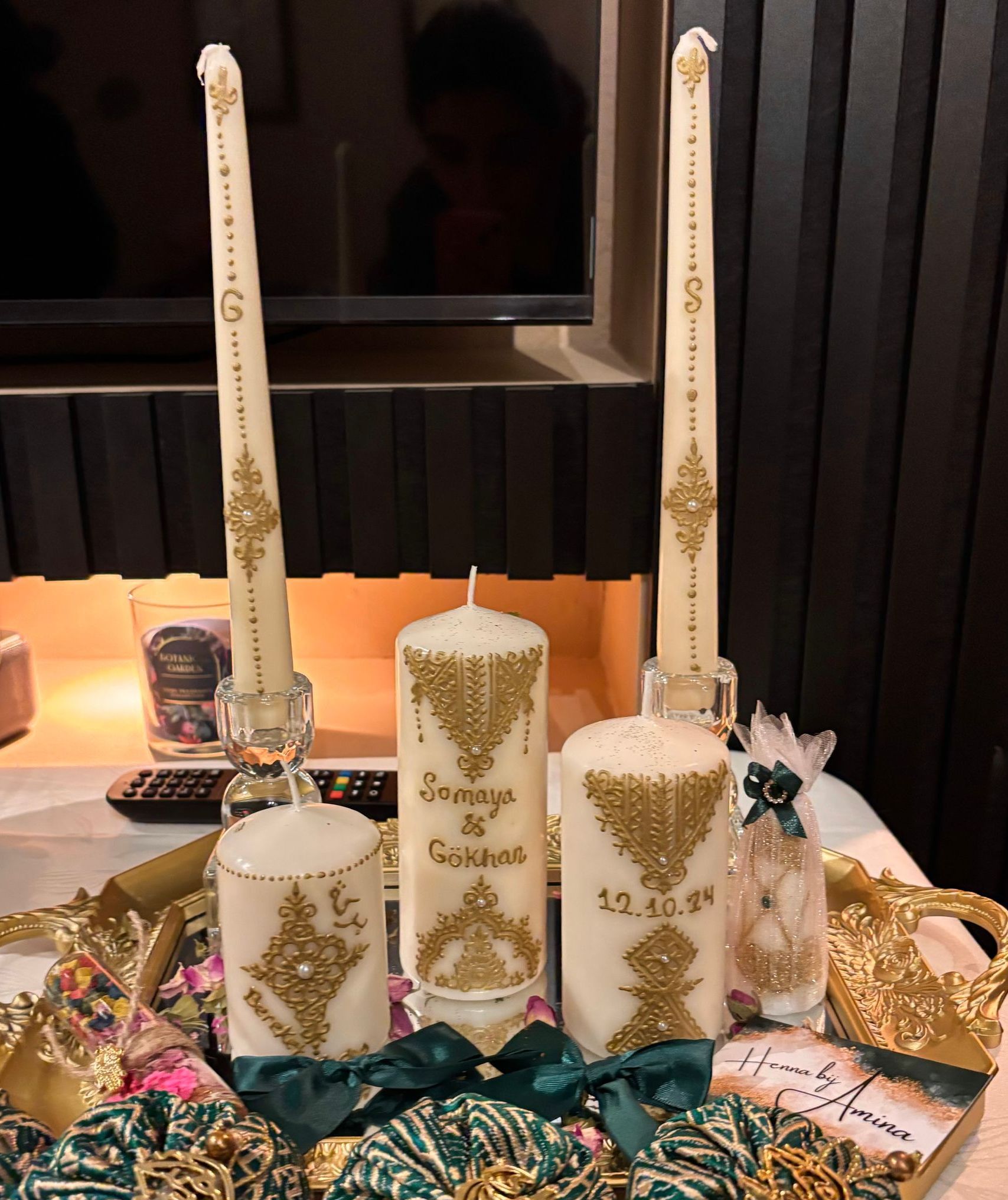 Kaarsen met gouden versieringen en letters, gerangschikt op een dienblad met linten en een klein cadeautje.