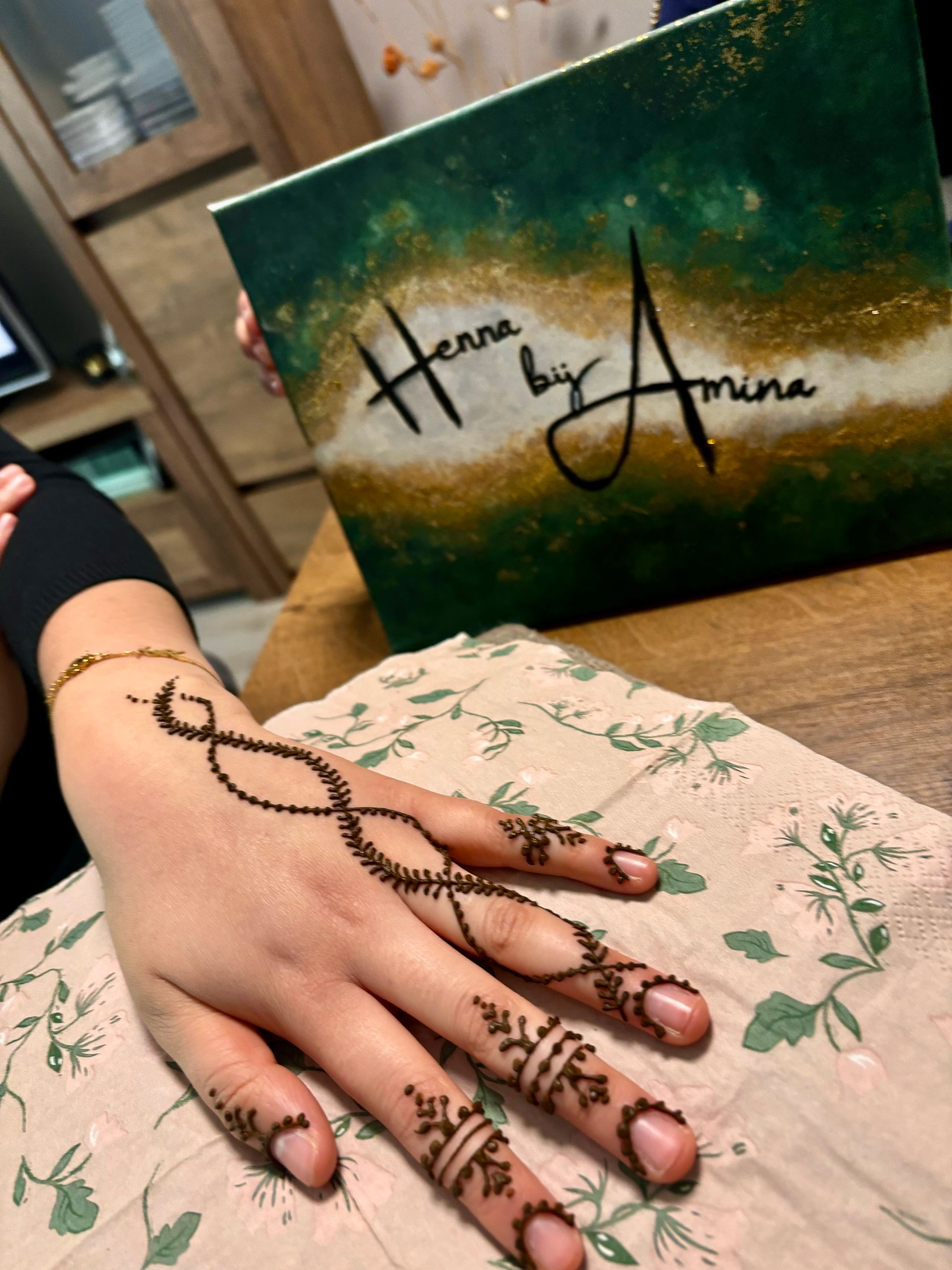 Hand met henna-ontwerp en groen, goudkleurig canvas met de tekst 
