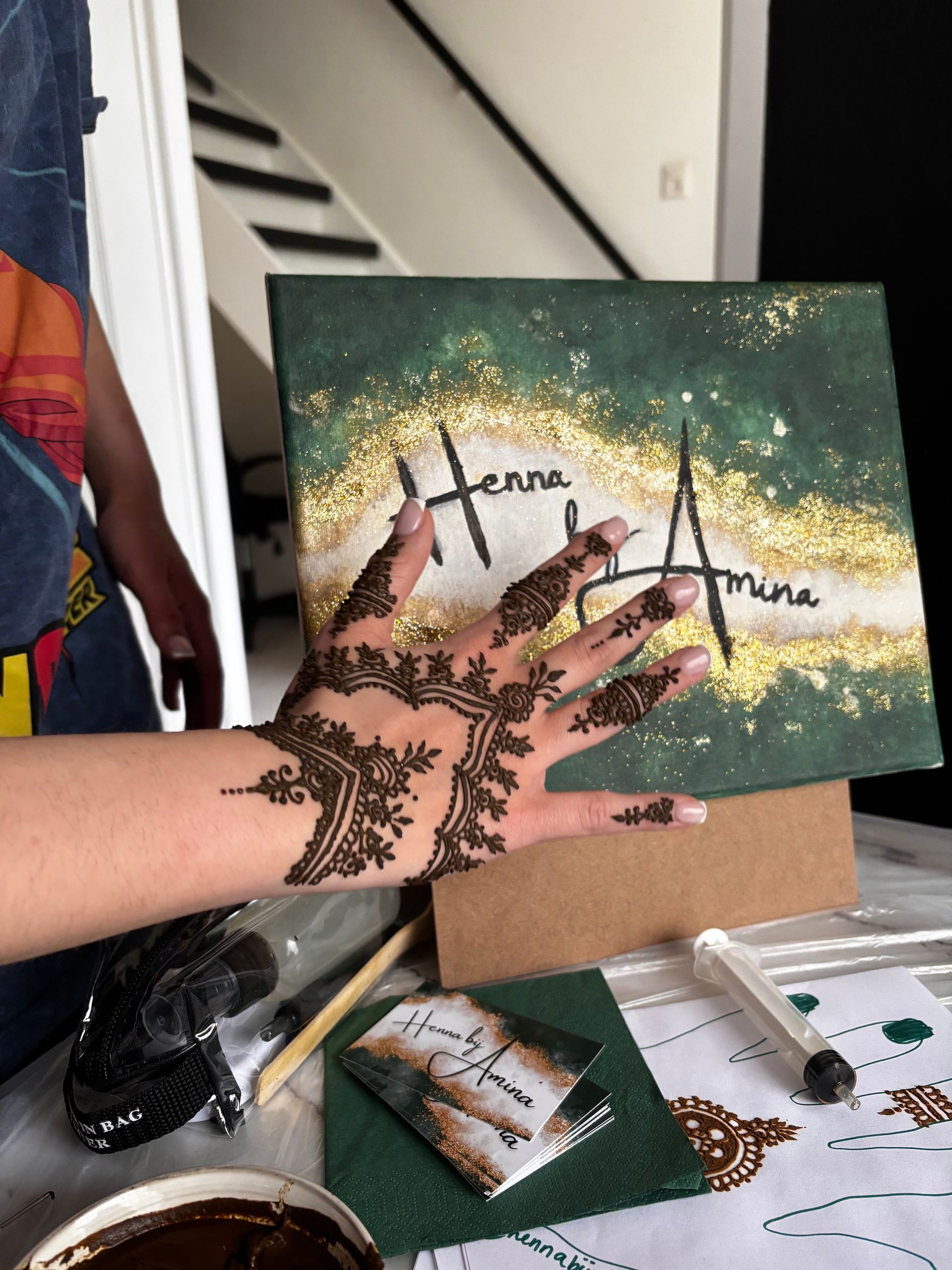 Hand met henna-ontwerp over een schilderij. Schilderij met gouden glitter, groene verf en tekst.