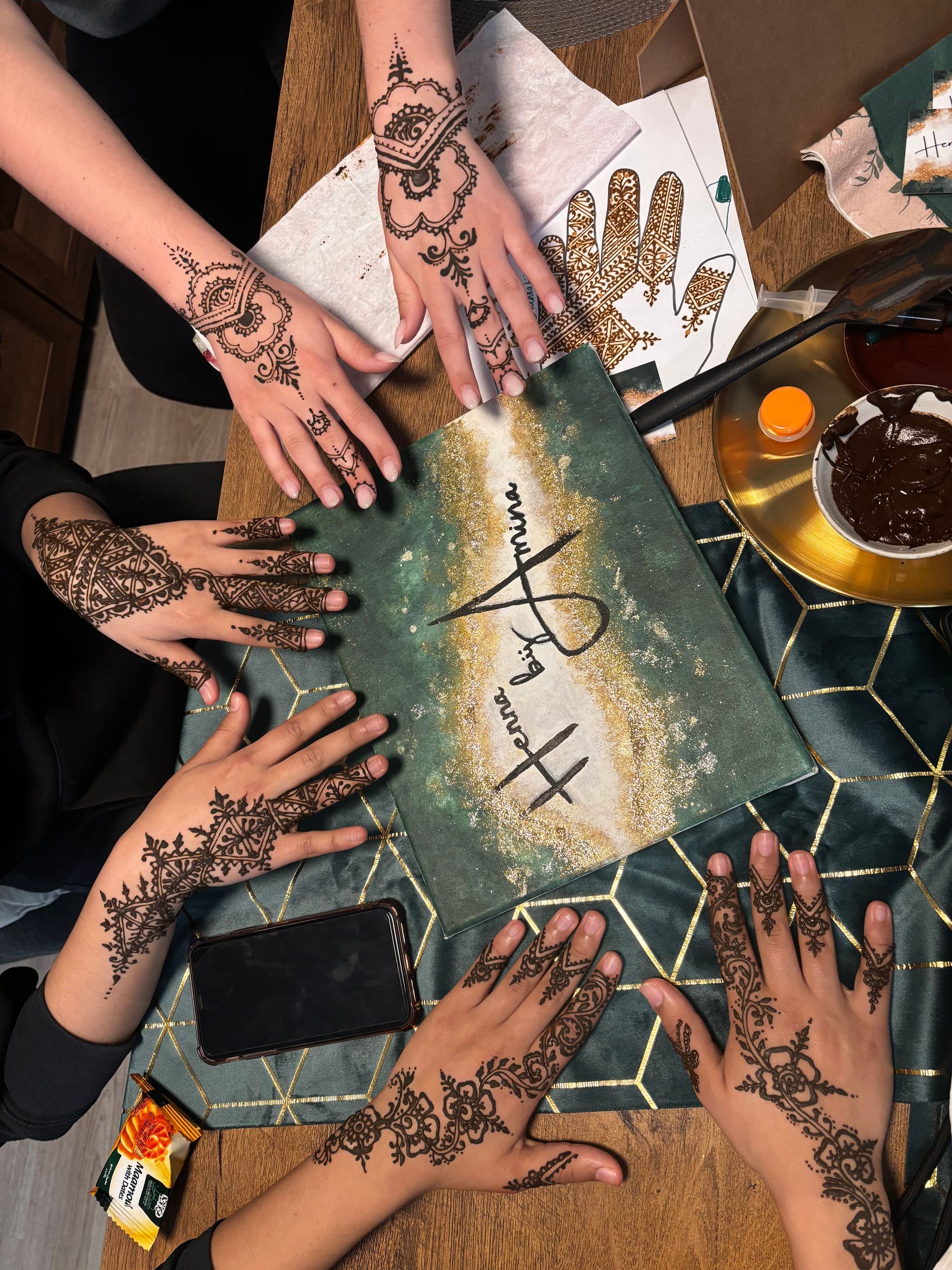 Handen met henna-ontwerpen rond een decoratieve tafel.