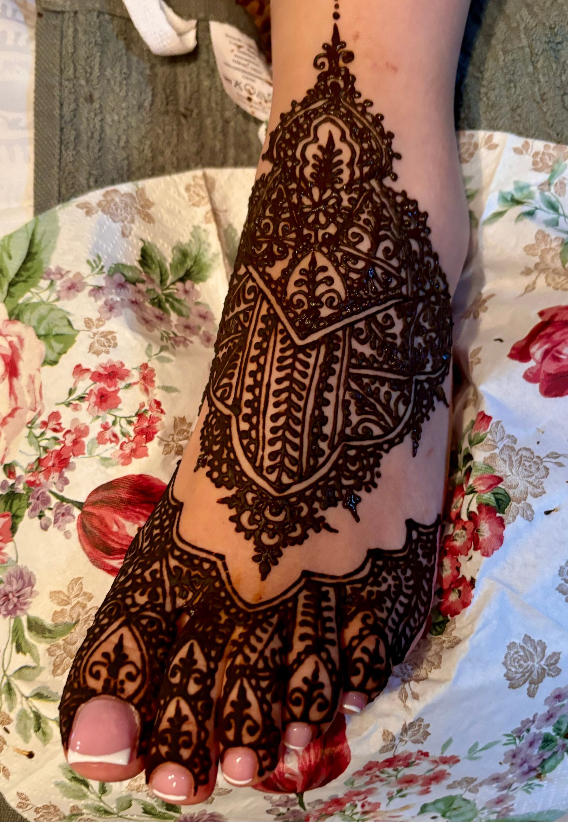 Voet met uitgebreid henna-ontwerp op de bovenkant, tenen met witte nagellak op de punten, achtergrond van bloemenstof.