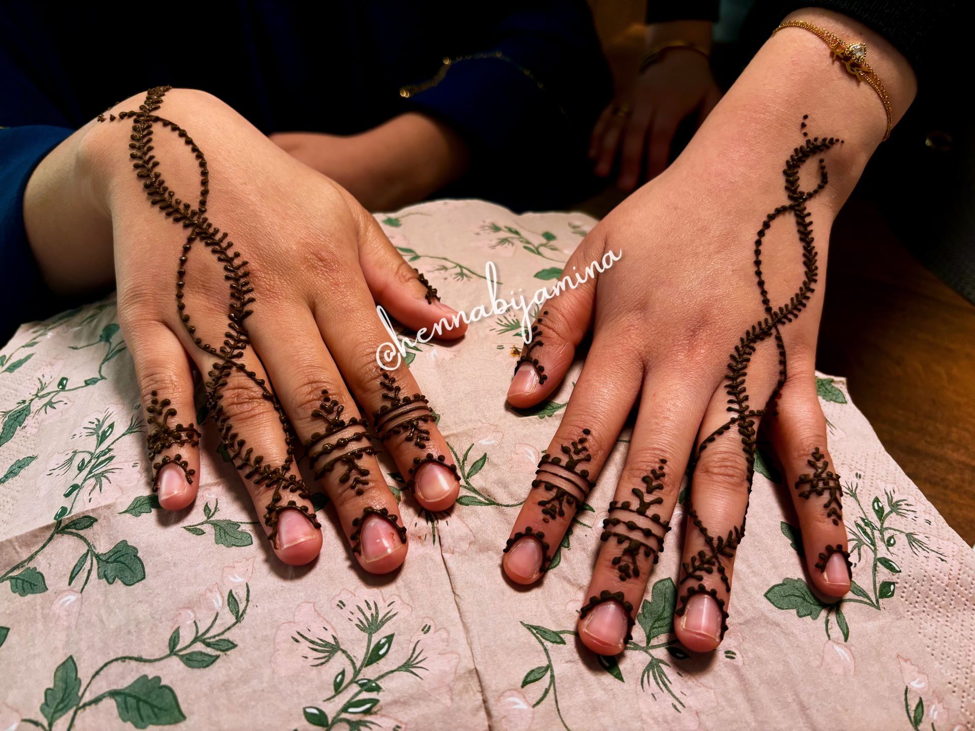 Handen met ingewikkelde henna-ontwerpen in het zwart, op een doek met bloemenmotief.
