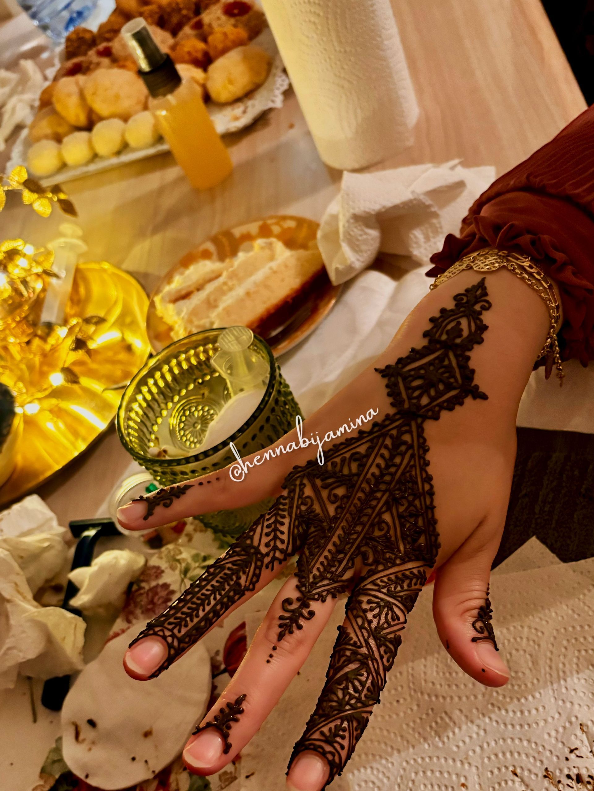 Hand met ingewikkeld henna-ontwerp, gouden armband en eten op de achtergrond.