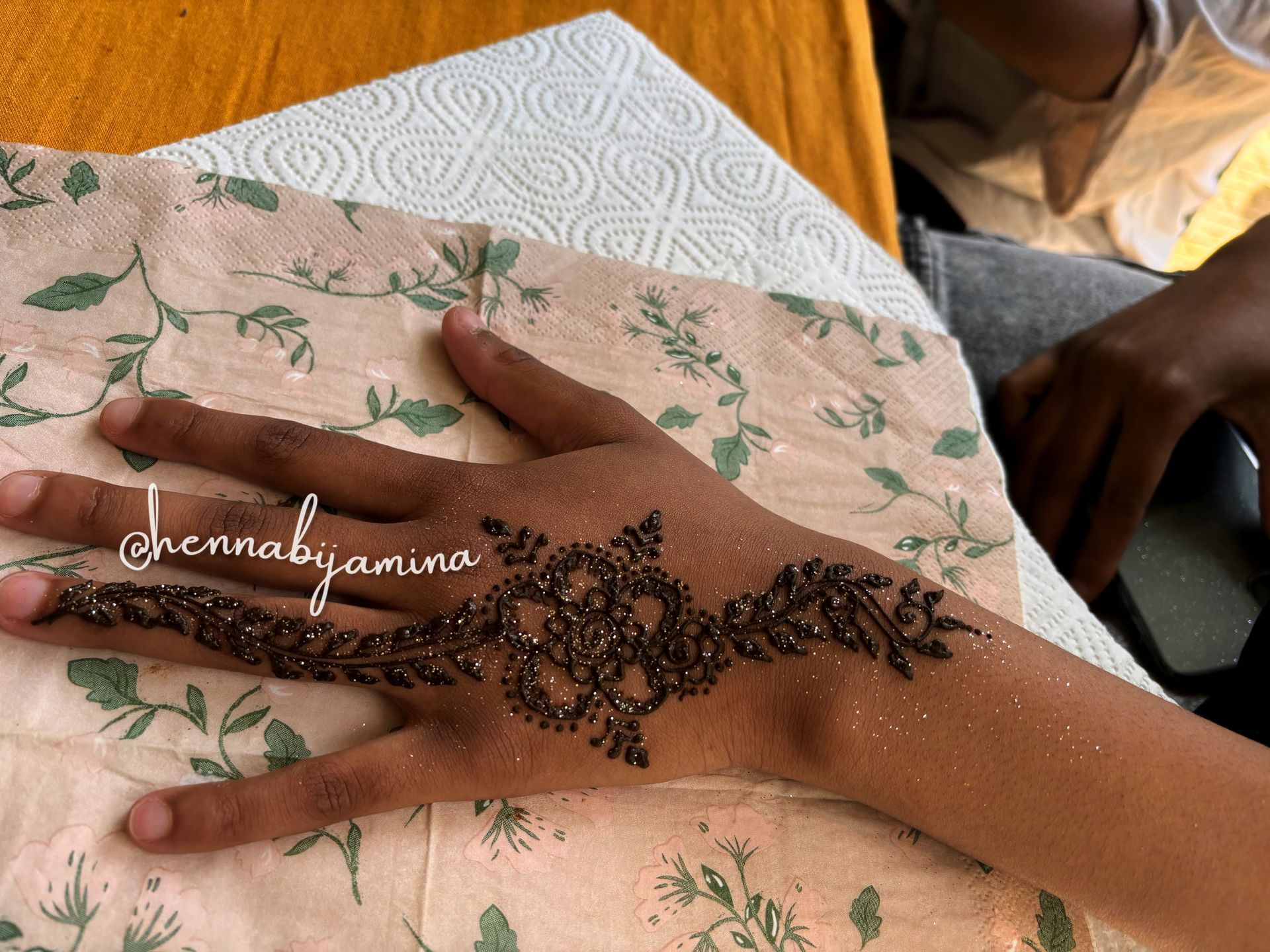 Hand met henna-tatoeage op een bloemenpatroonpapier. Donkerbruin henna-ontwerp, bladeren en bloemen.
