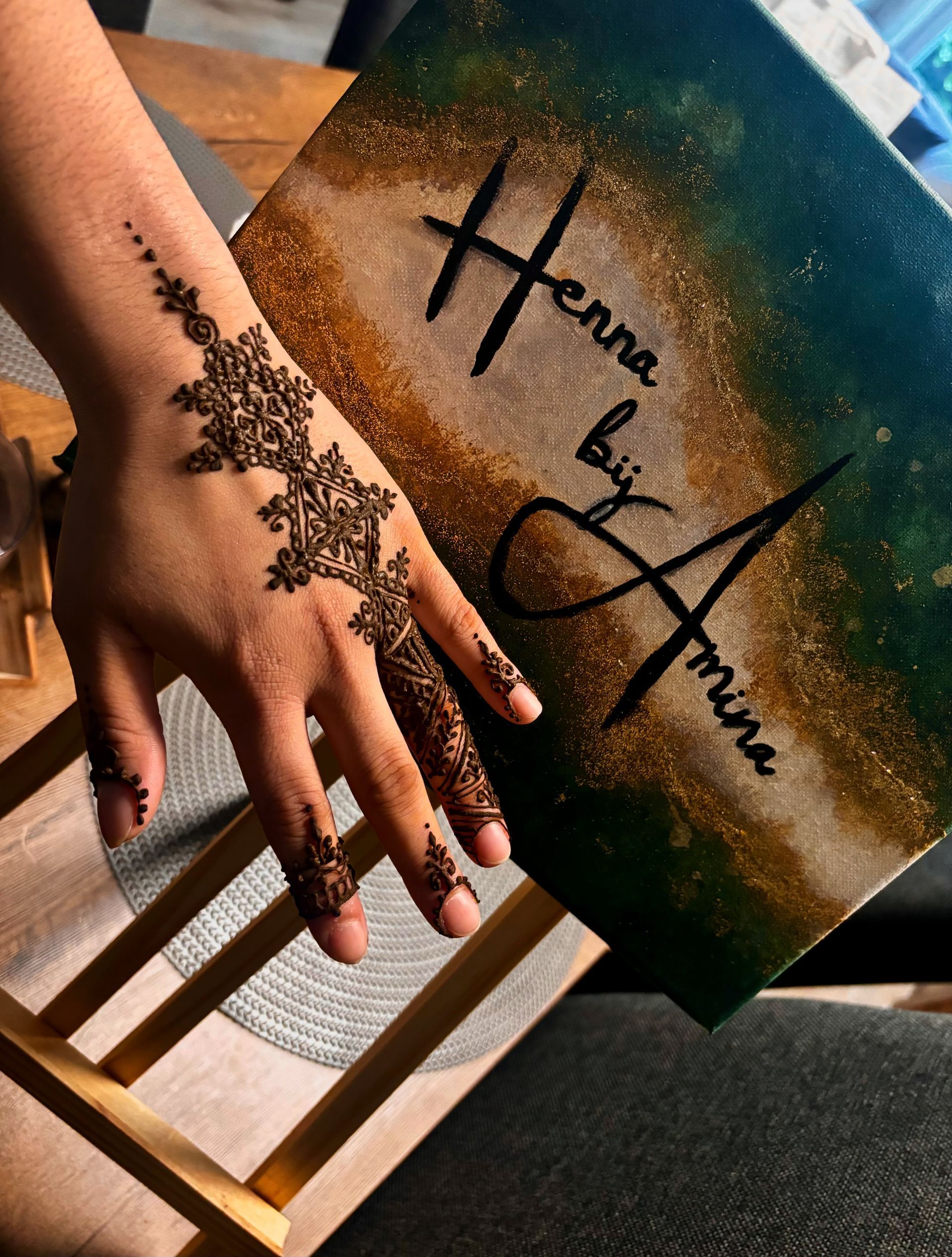 Hand met henna-ontwerp naast een canvas met de tekst “Henna door Amira.”