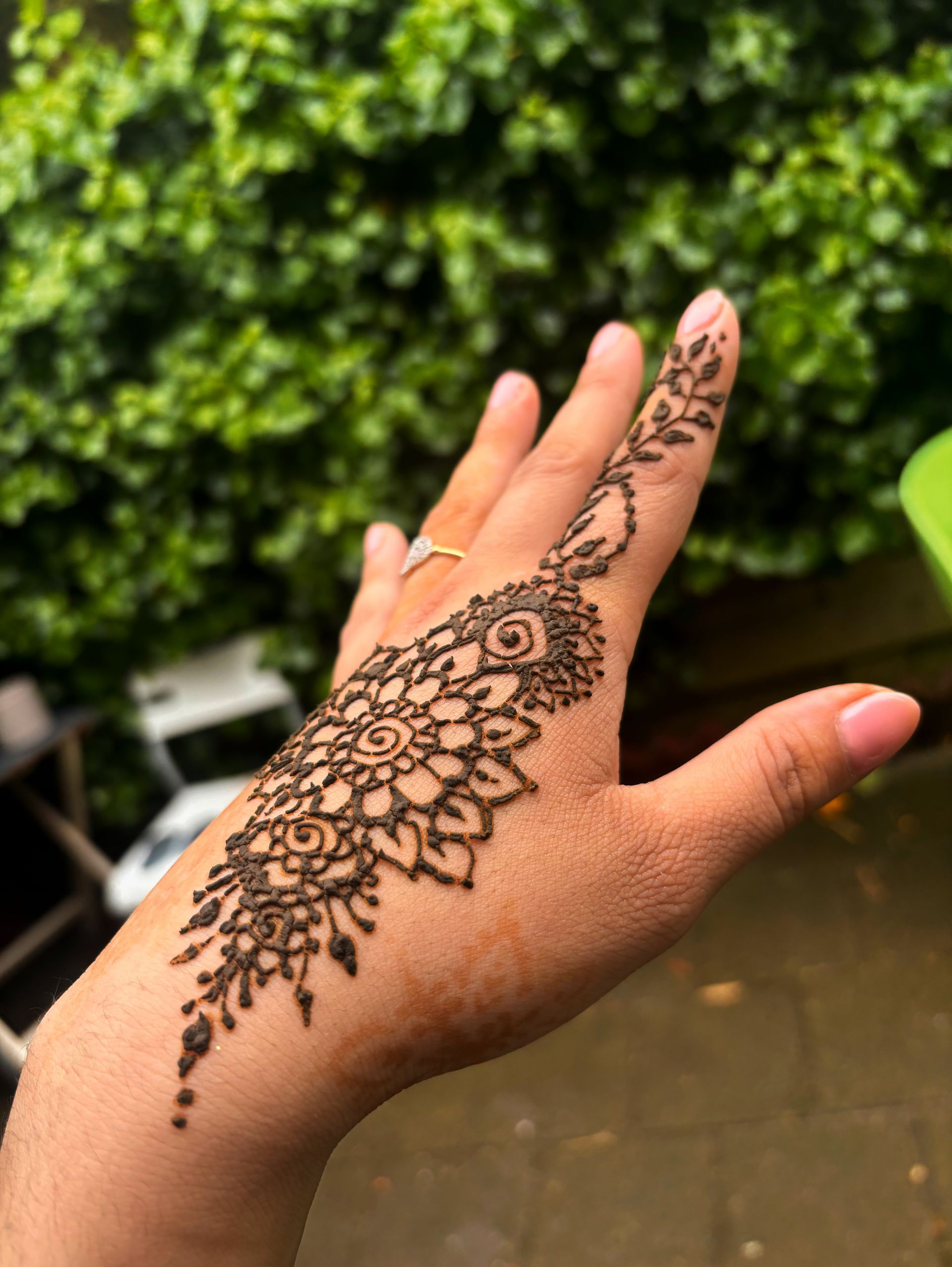 Hand met ingewikkeld henna-ontwerp tegen een groene bladachtergrond.