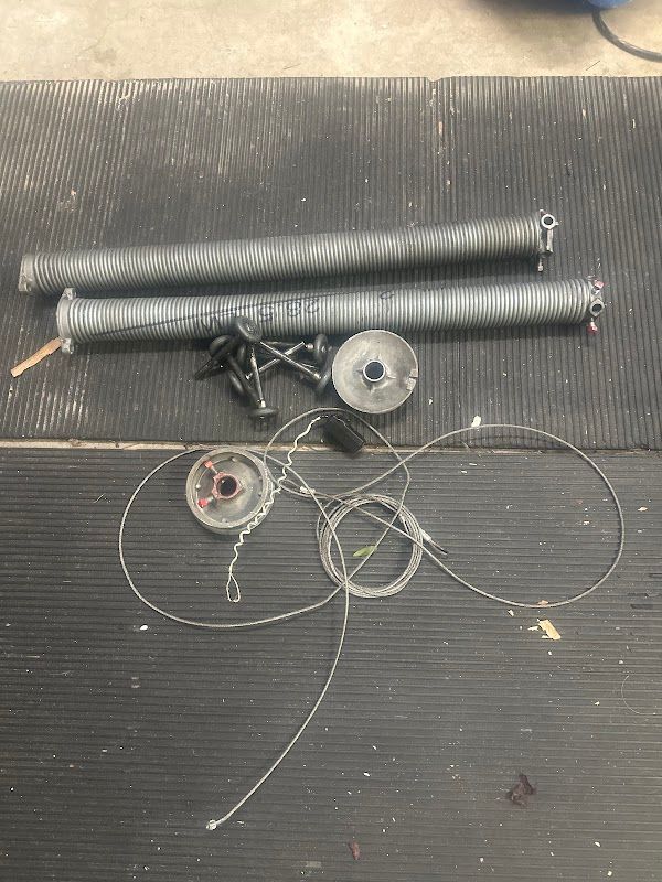 Two garage door torsion springs, cable drums and lift cables laid out during service
