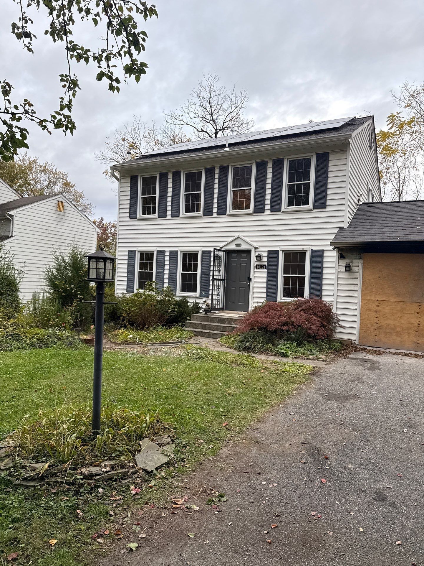 Boarded-up white house exterior with damaged roof and trees nearby