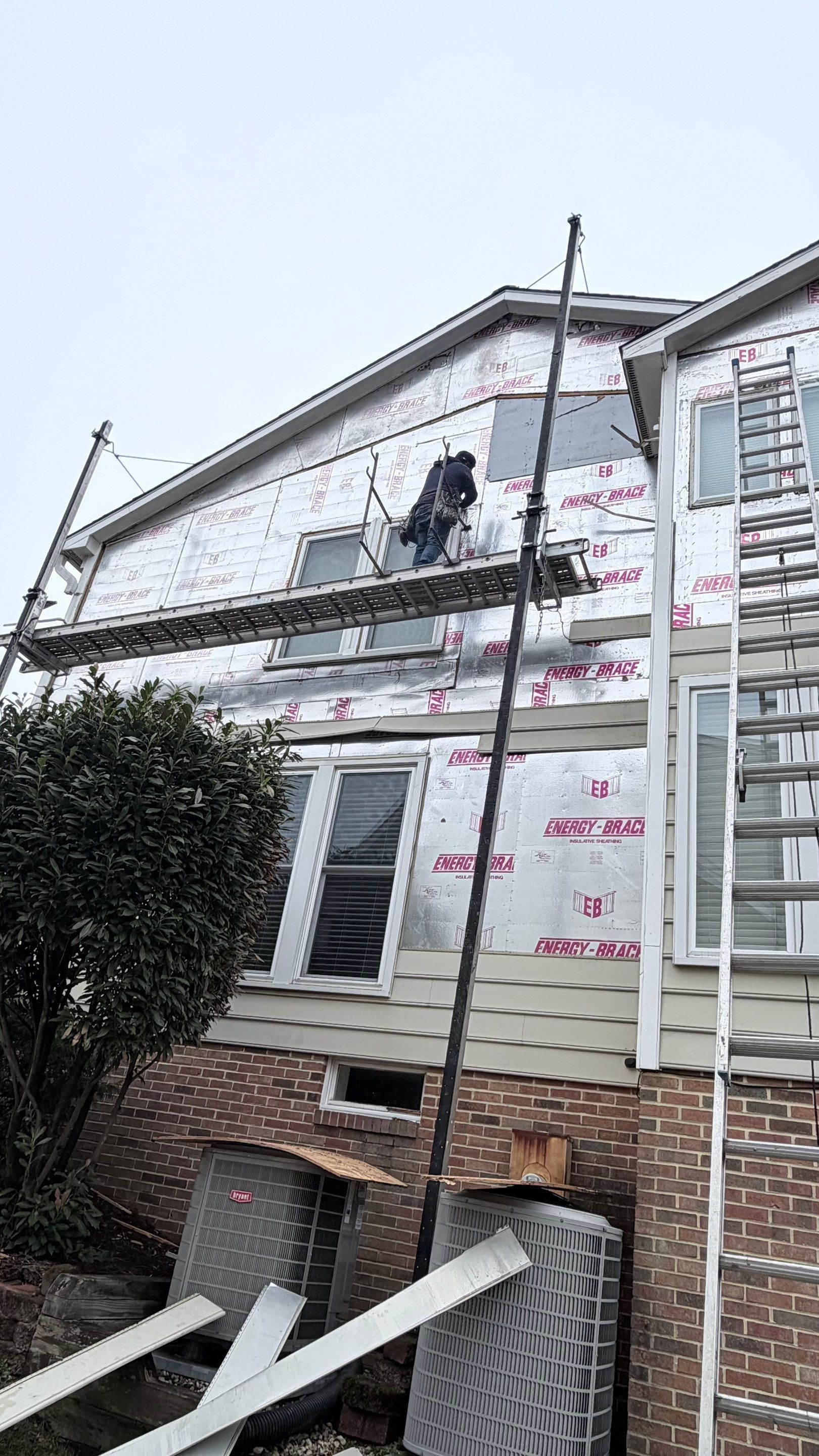 House exterior under construction with scaffolding and wrapped siding panels