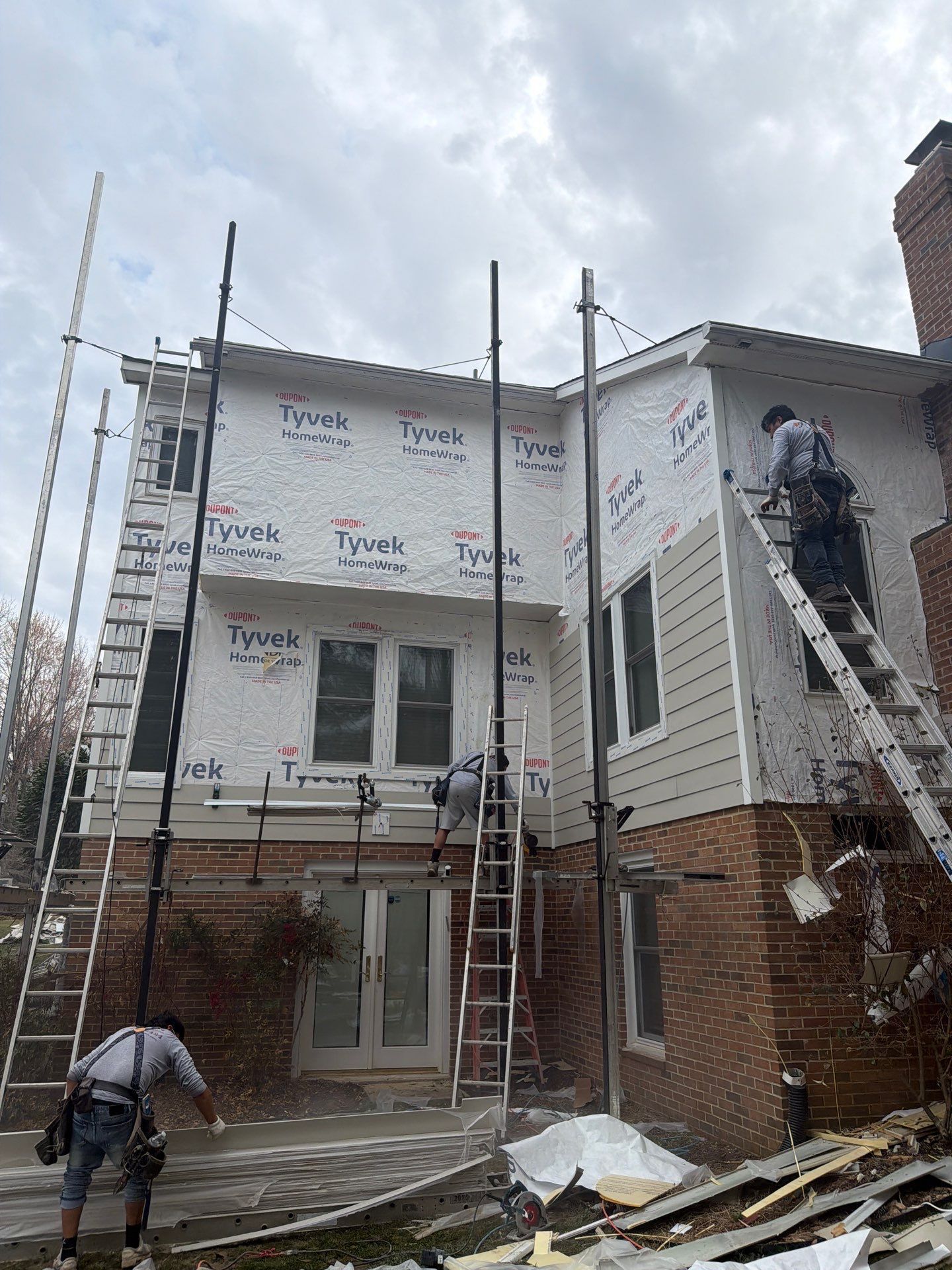 Workers on scaffolding renovating a house exterior, with siding and roof repairs in progress.