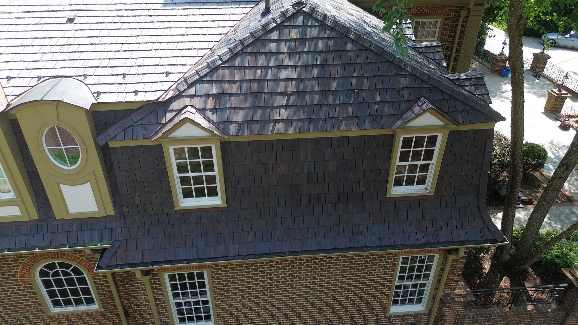 Aerial view of a gray-shingled house roof with dormer windows and stone exterior walls.