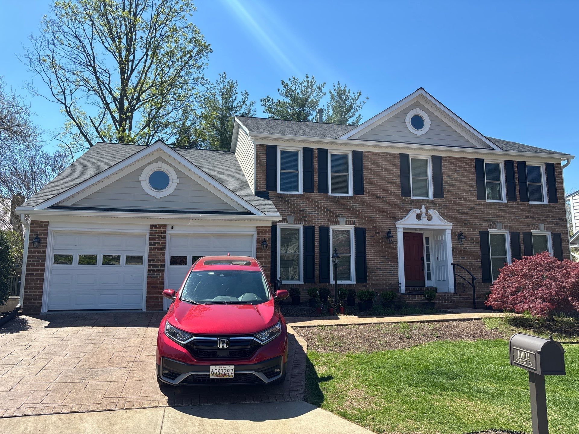 Suburban two-story brick house with white garage and a red SUV parked in the driveway.