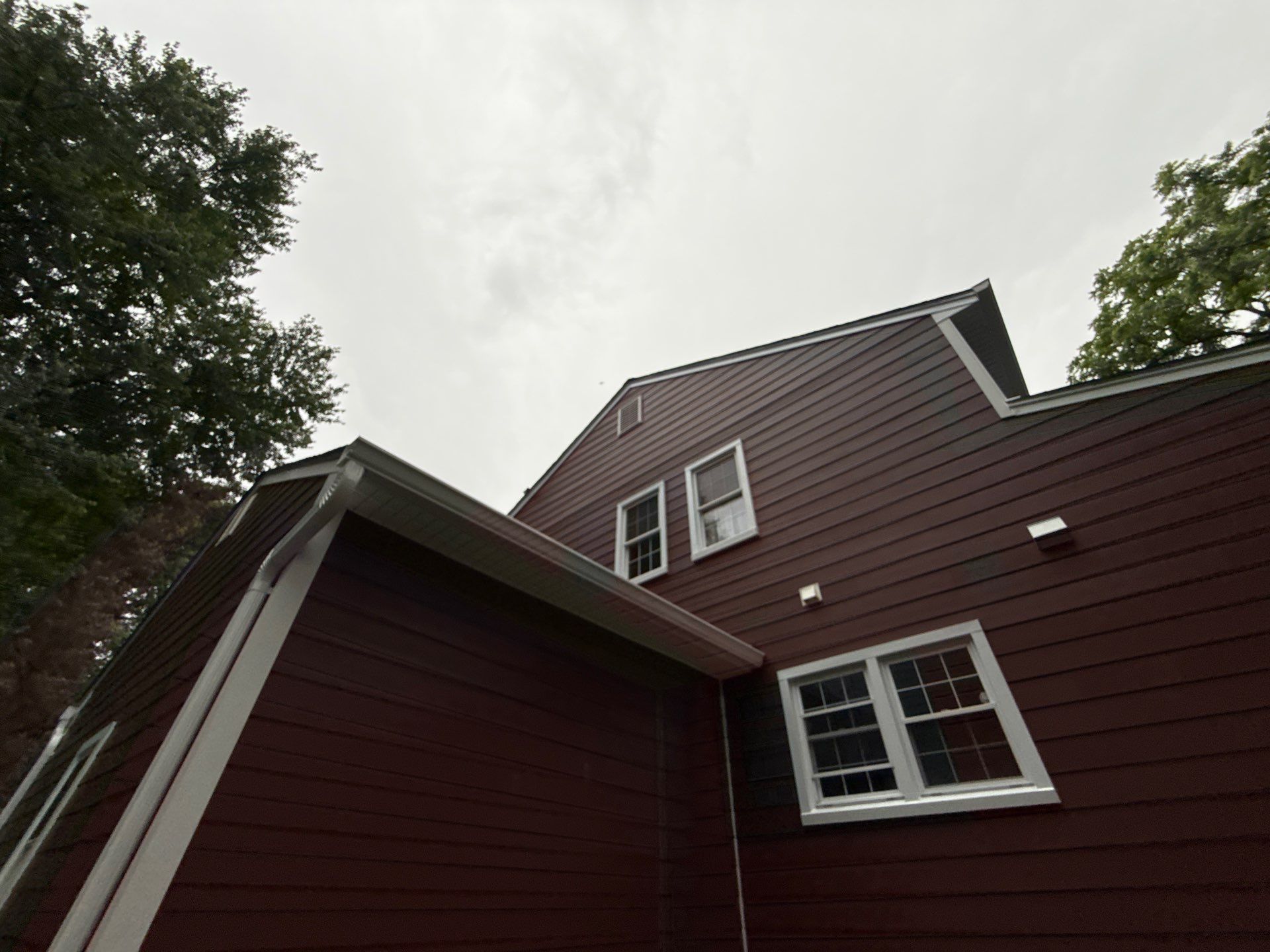 Red house exterior with white trim and dormer windows under a cloudy sky