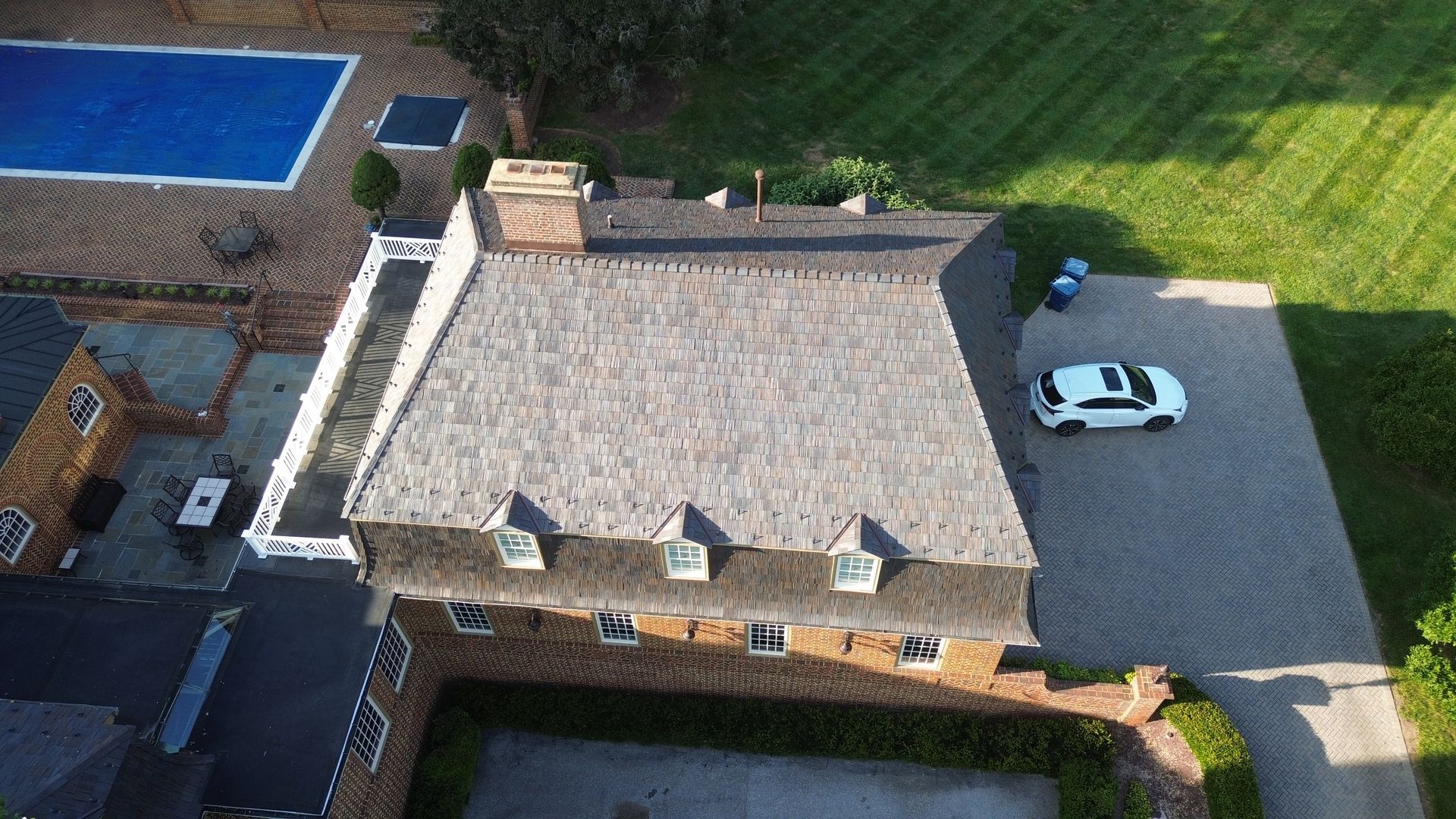 Aerial view of a stone-roofed house with a white car parked beside it and a blue pool nearby.
