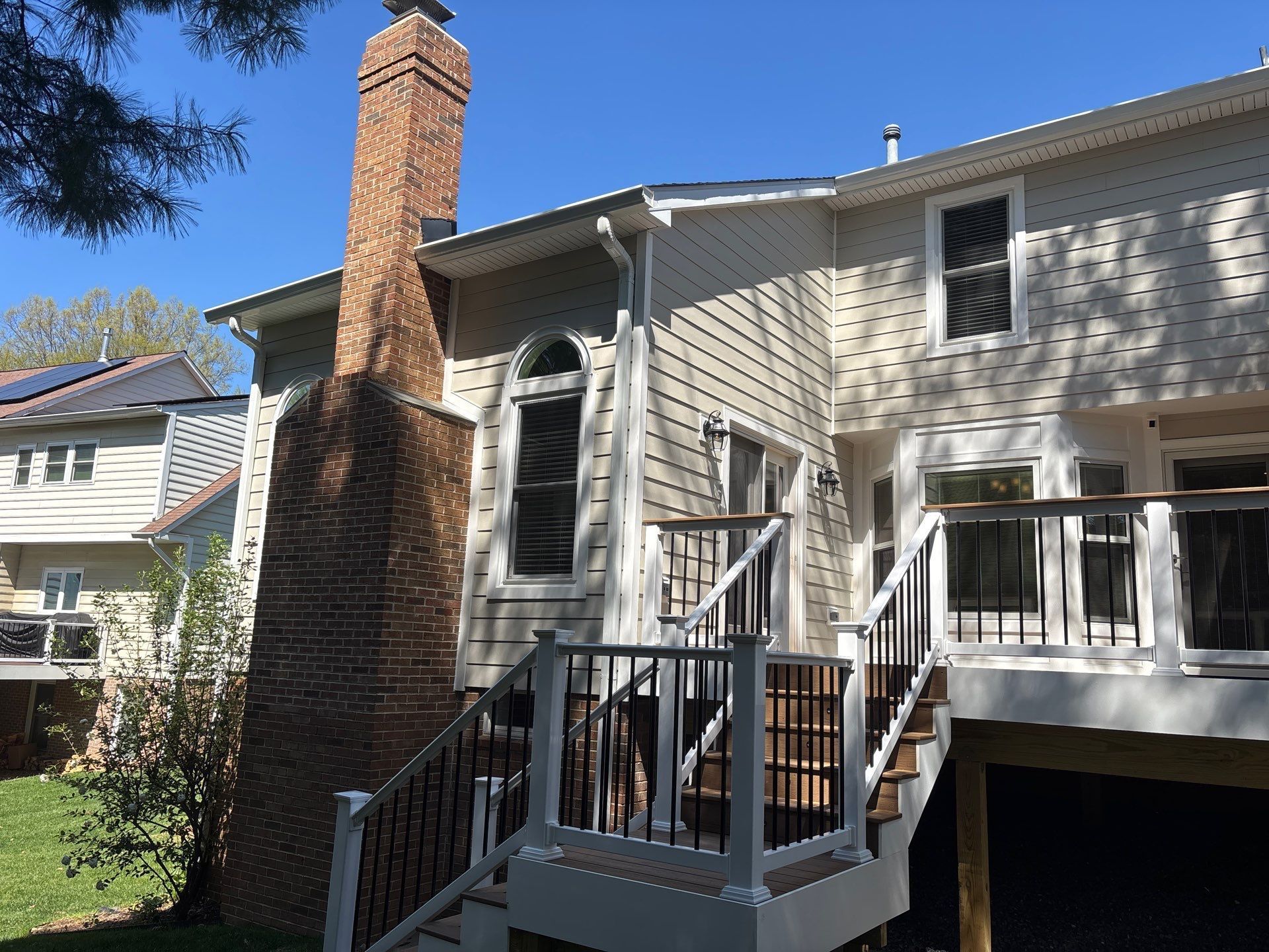 Back deck and stairs beside a brick chimney on a beige townhouse exterior