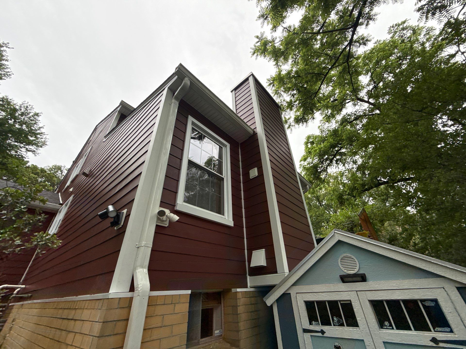 Red house exterior with tall chimney and white-trimmed windows beside a small blue garage.