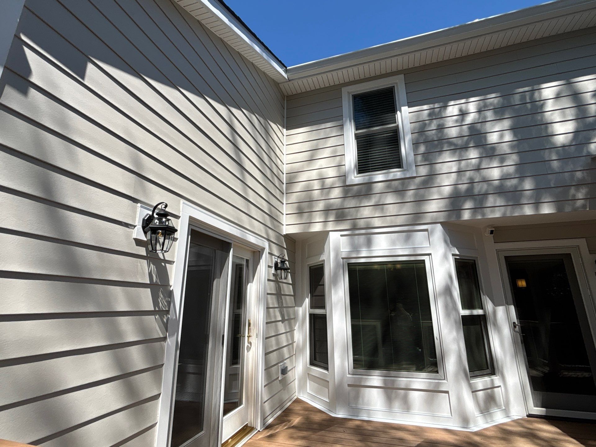 Exterior of a beige house with white trim, sliding glass door, windows, and a small patio area