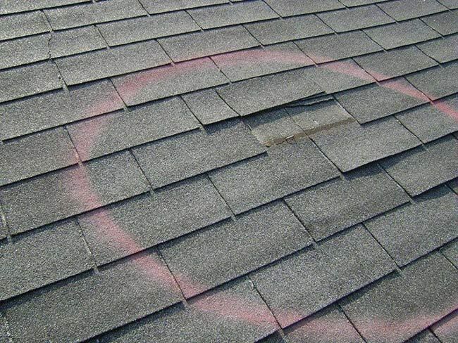 Gray asphalt roof shingles with pink chalk marking lines and a small damaged area