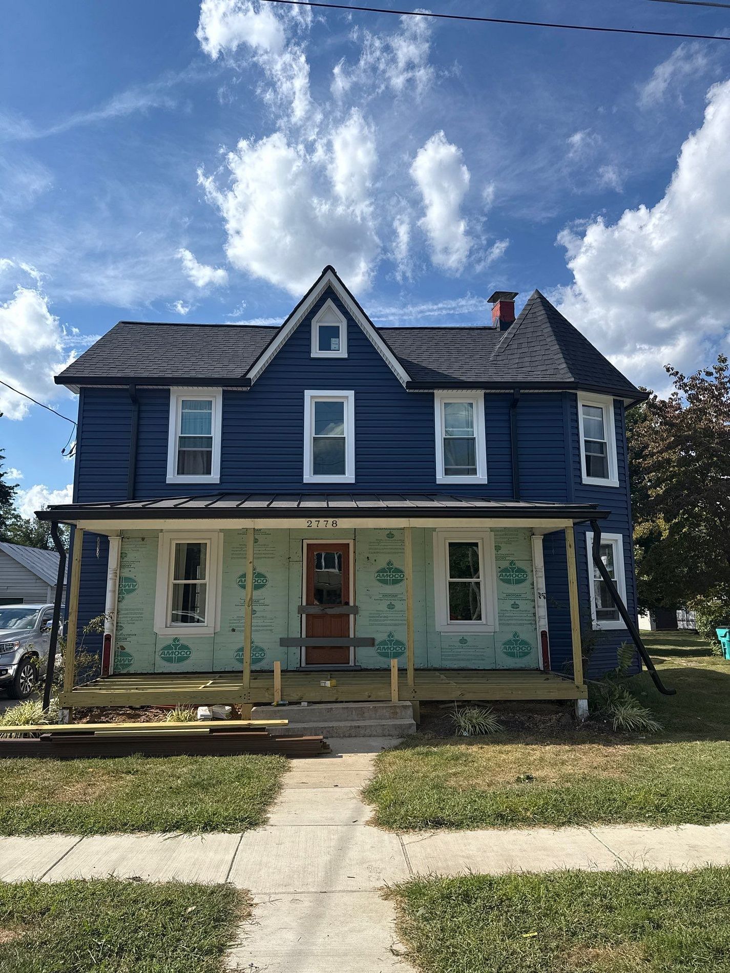 Blue two-story house with white trim and a front porch under a partly cloudy sky
