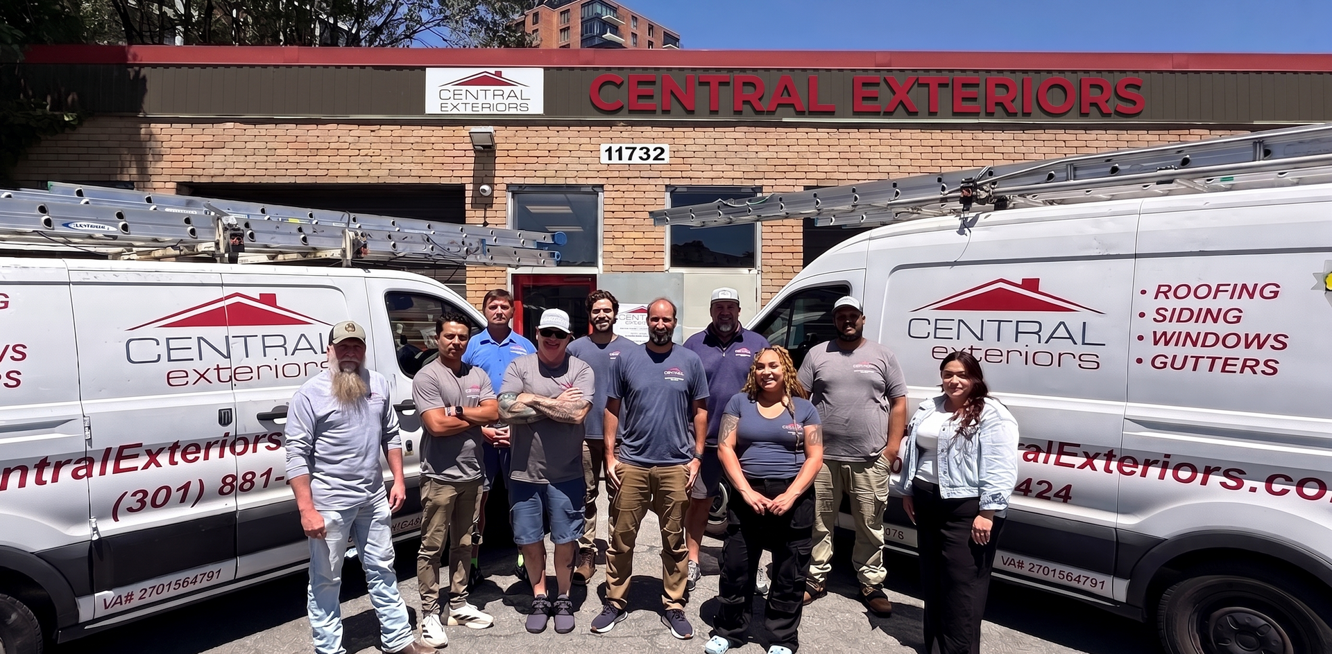 Group posing in front of Central Exteriors trucks and building, smiling on a sunny street.